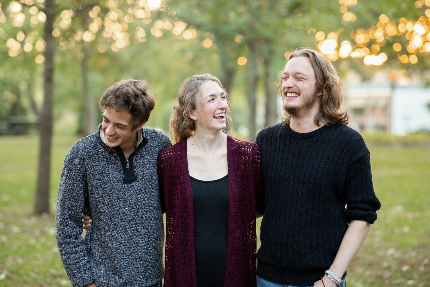 Three young people in casual sweaters smile and laugh together outdoors on an autumn day with golden bokeh background.