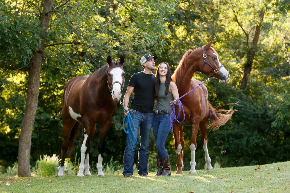 A couple and their horses laughing in sunlit wooded area.