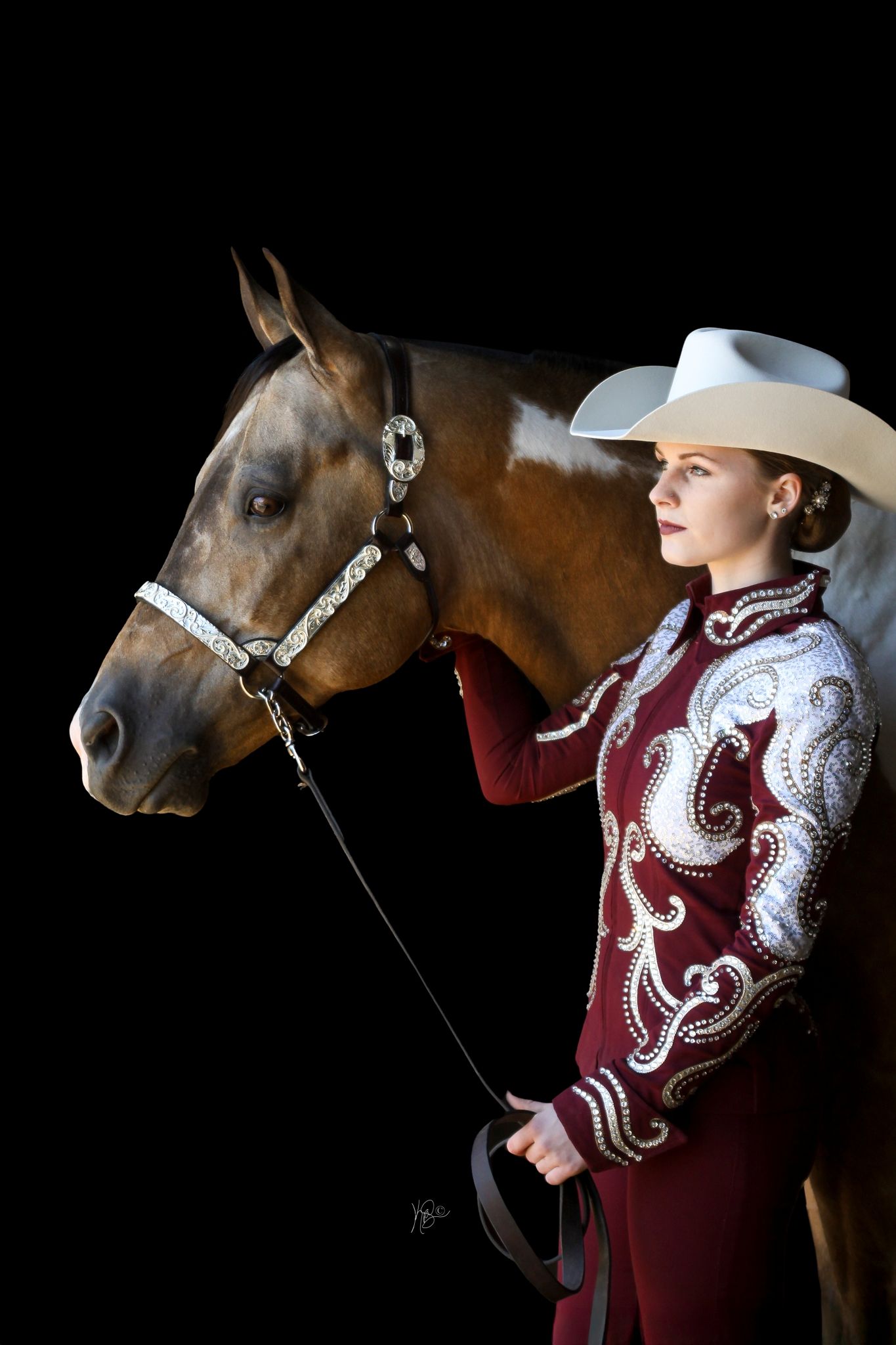 Horse and rider in elegant burgundy western show outfit against dark background.