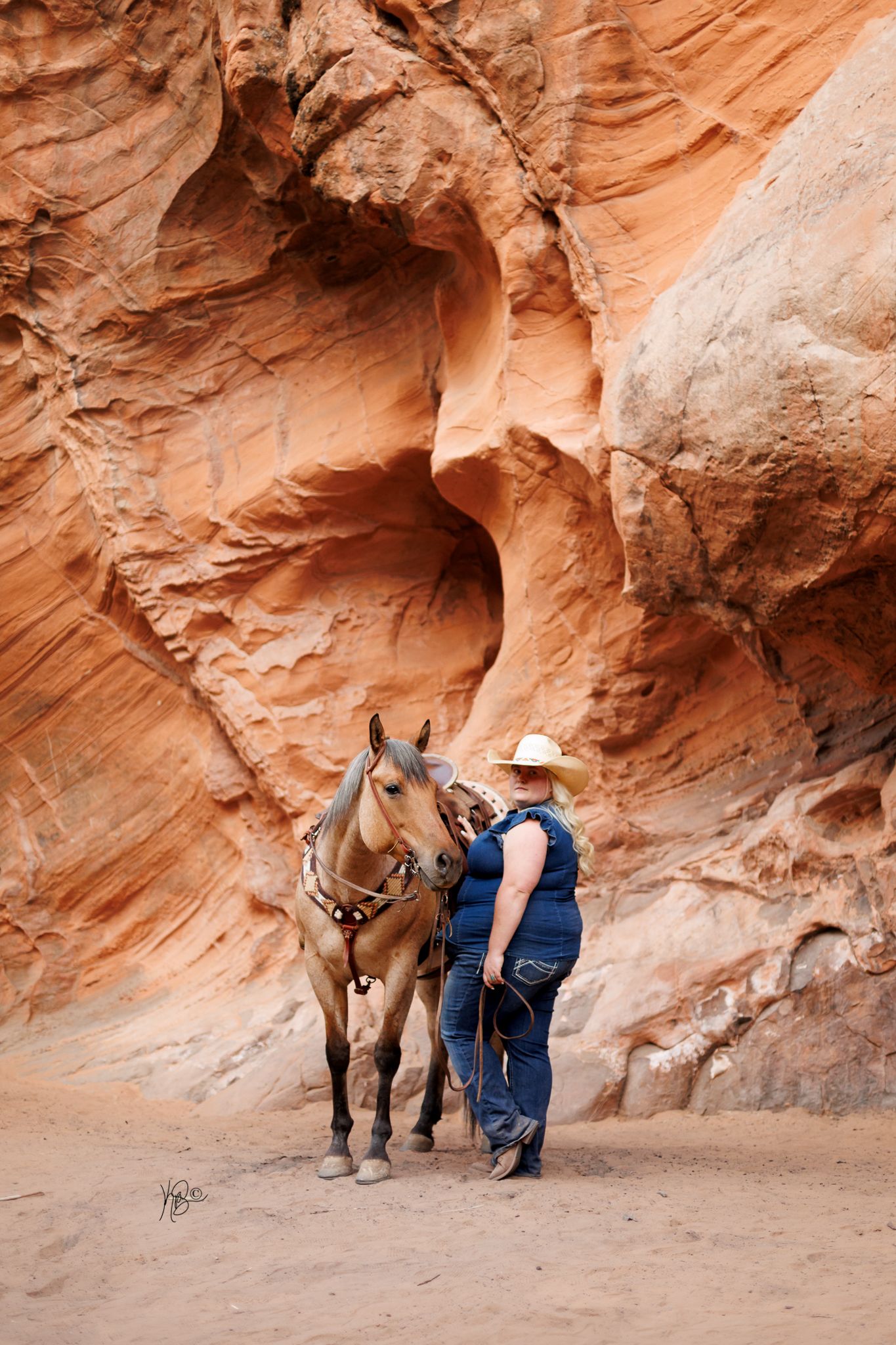 A woman standing for a portrait next to her western horse in a canyon-like setting.