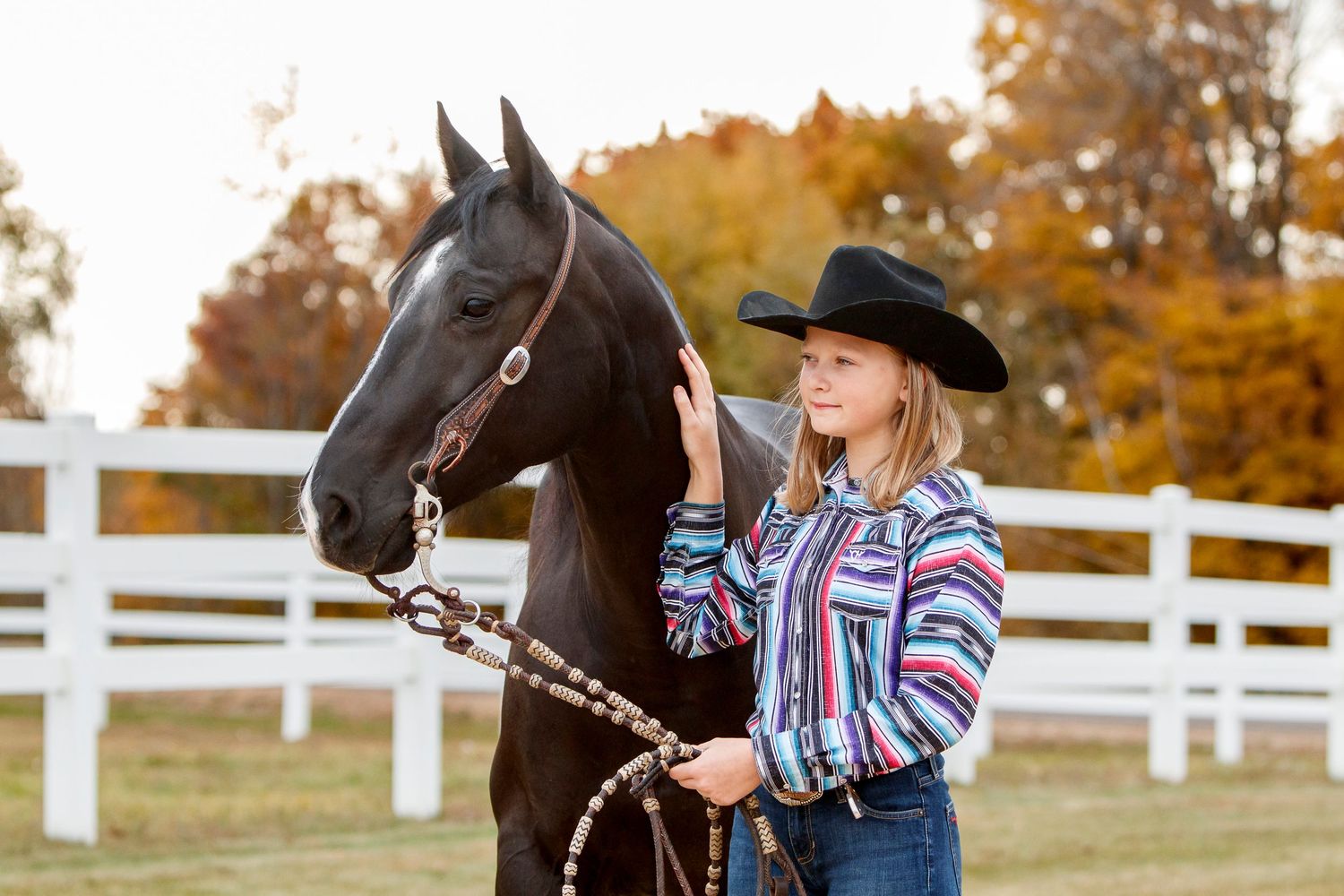 Horse and rider portrait standing near white fencing during golden autumn sunset.