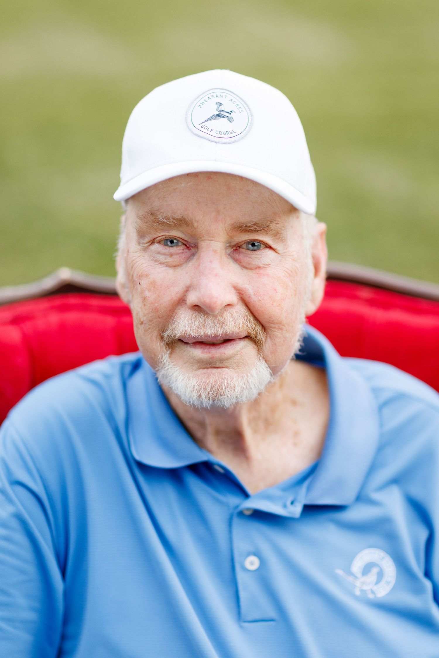 Senior man in blue polo shirt and white cap smiles warmly at camera.