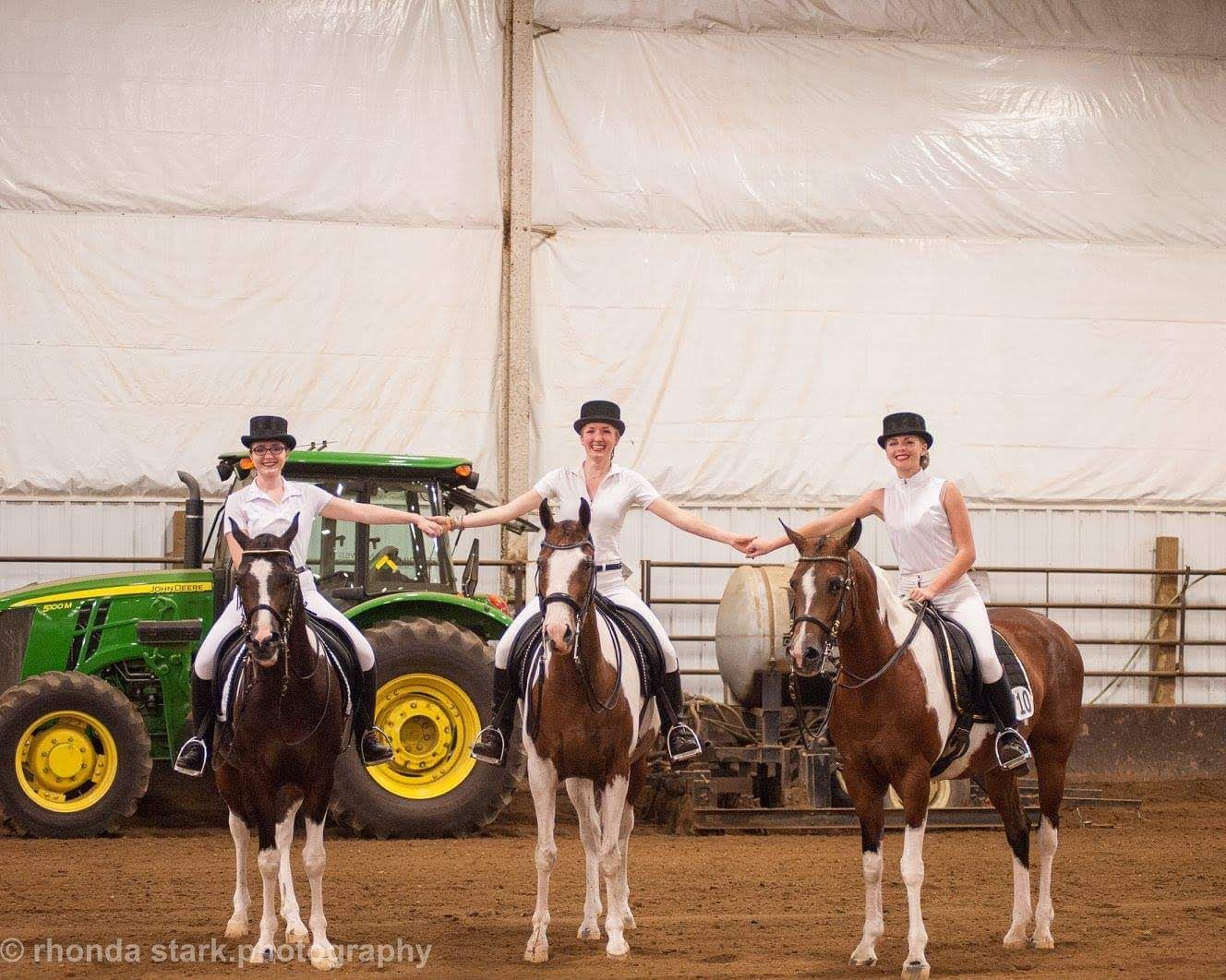 Line of riders on horses holding hands in an indoor arena at a horse show.