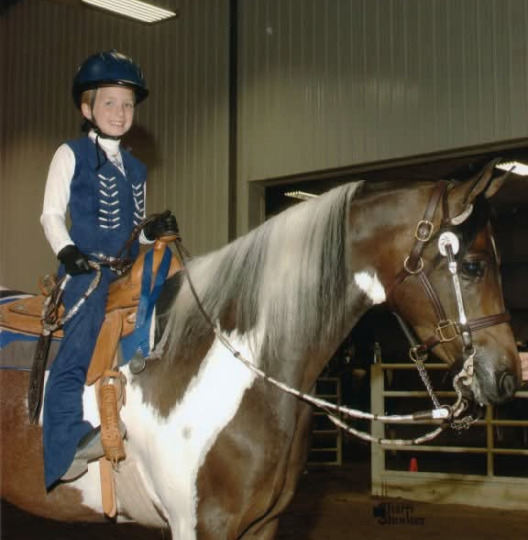 Little girl on a pinto horse and dressed in western show attire.