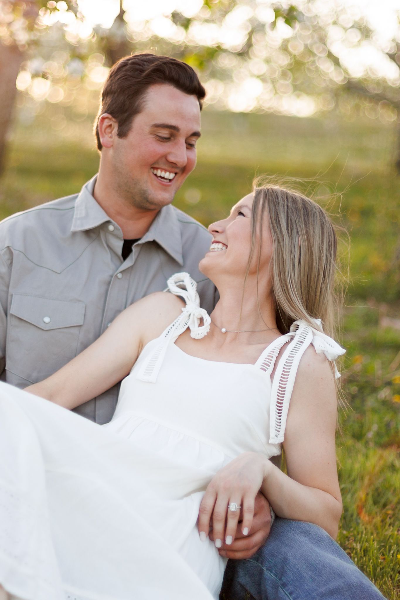 Romantic couple laughing together in a sunny field, the young woman wearing a white dress.