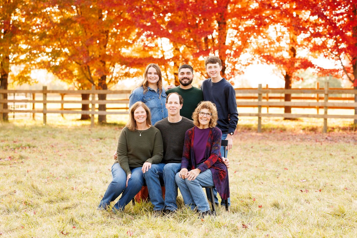 Family portrait session in a golden autumn field with rustic wooden fence at sunset.