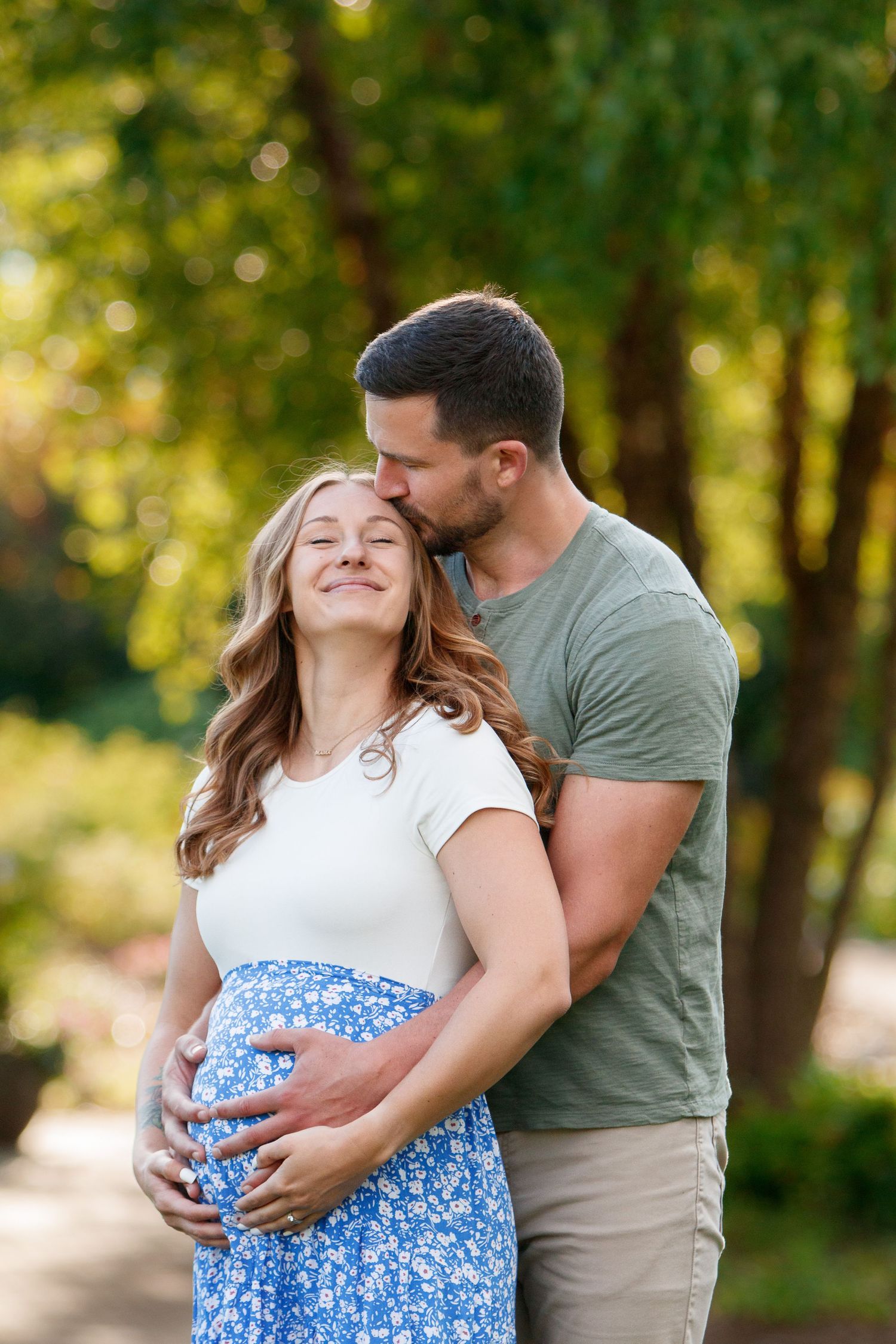 Couple embraces in a romantic maternity photoshoot outdoors with white and blue floral outfits.