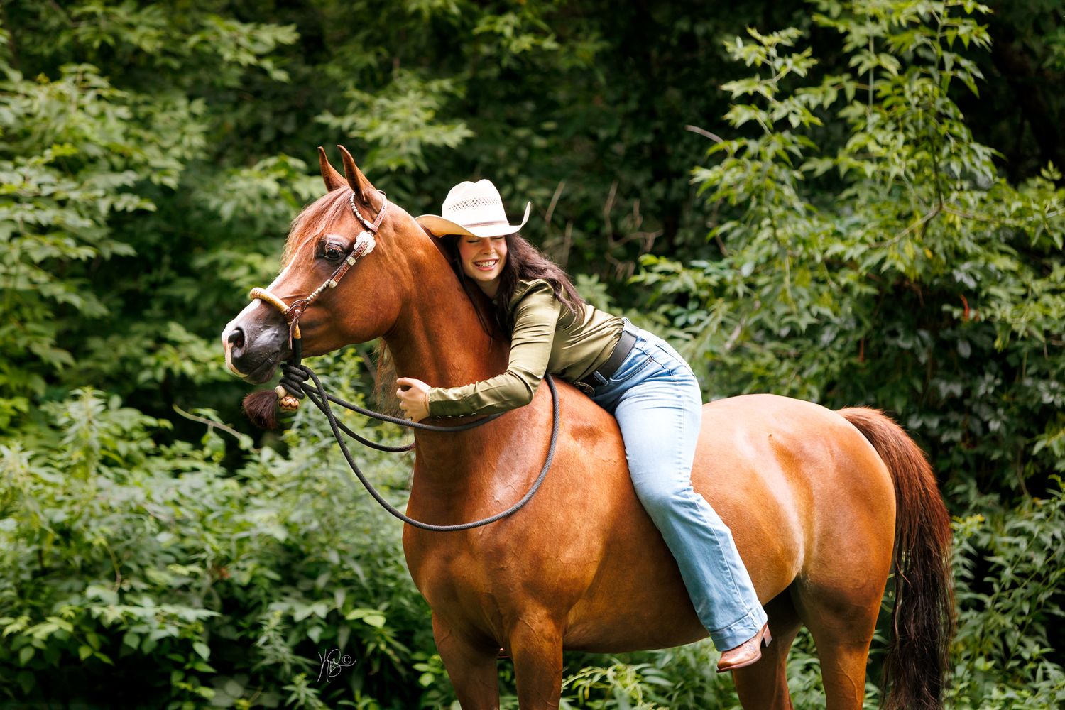Western rider bareback on her chestnut horse and hugging their neck against a forest setting.