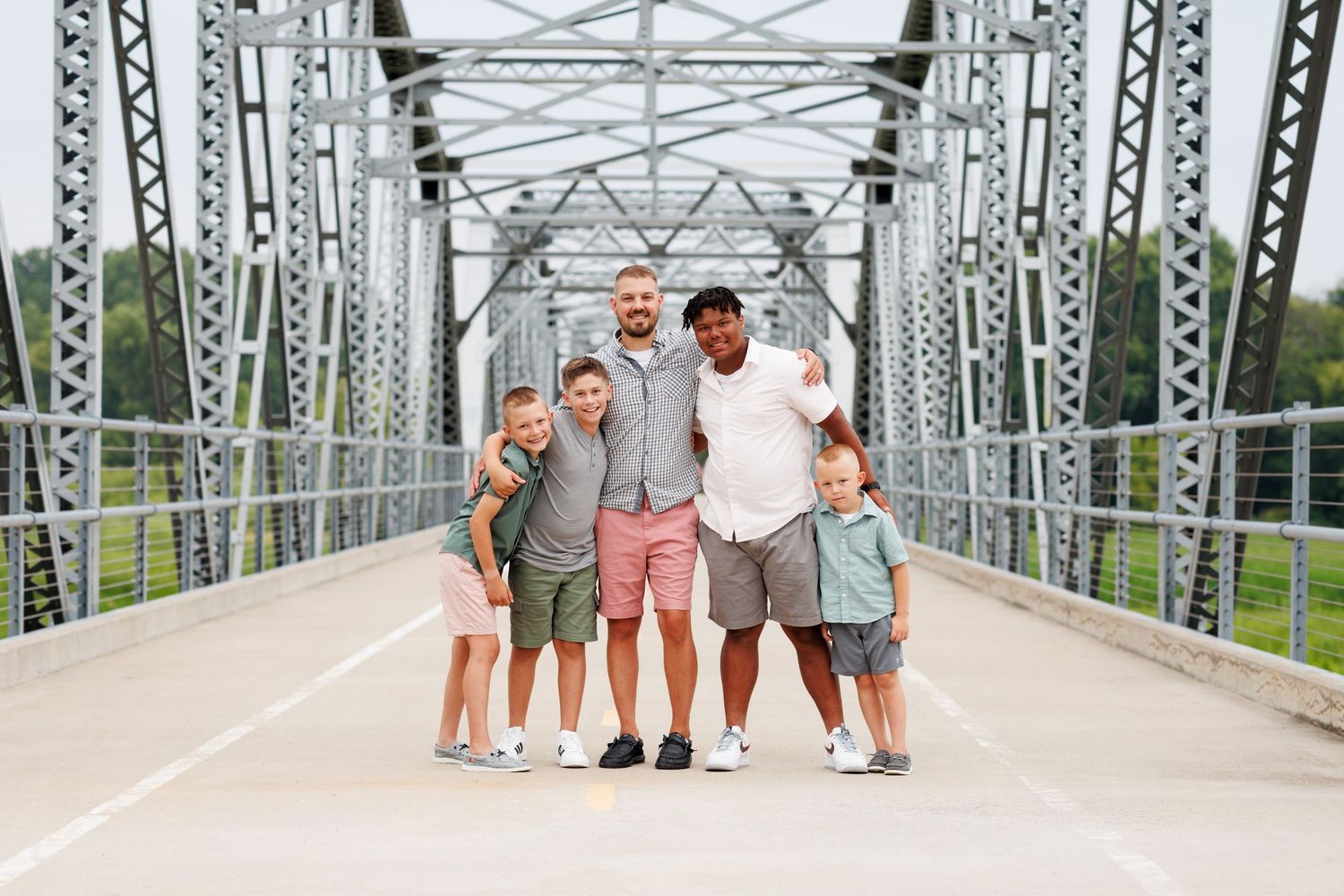 Family of five posing together on a steel bridge structure.