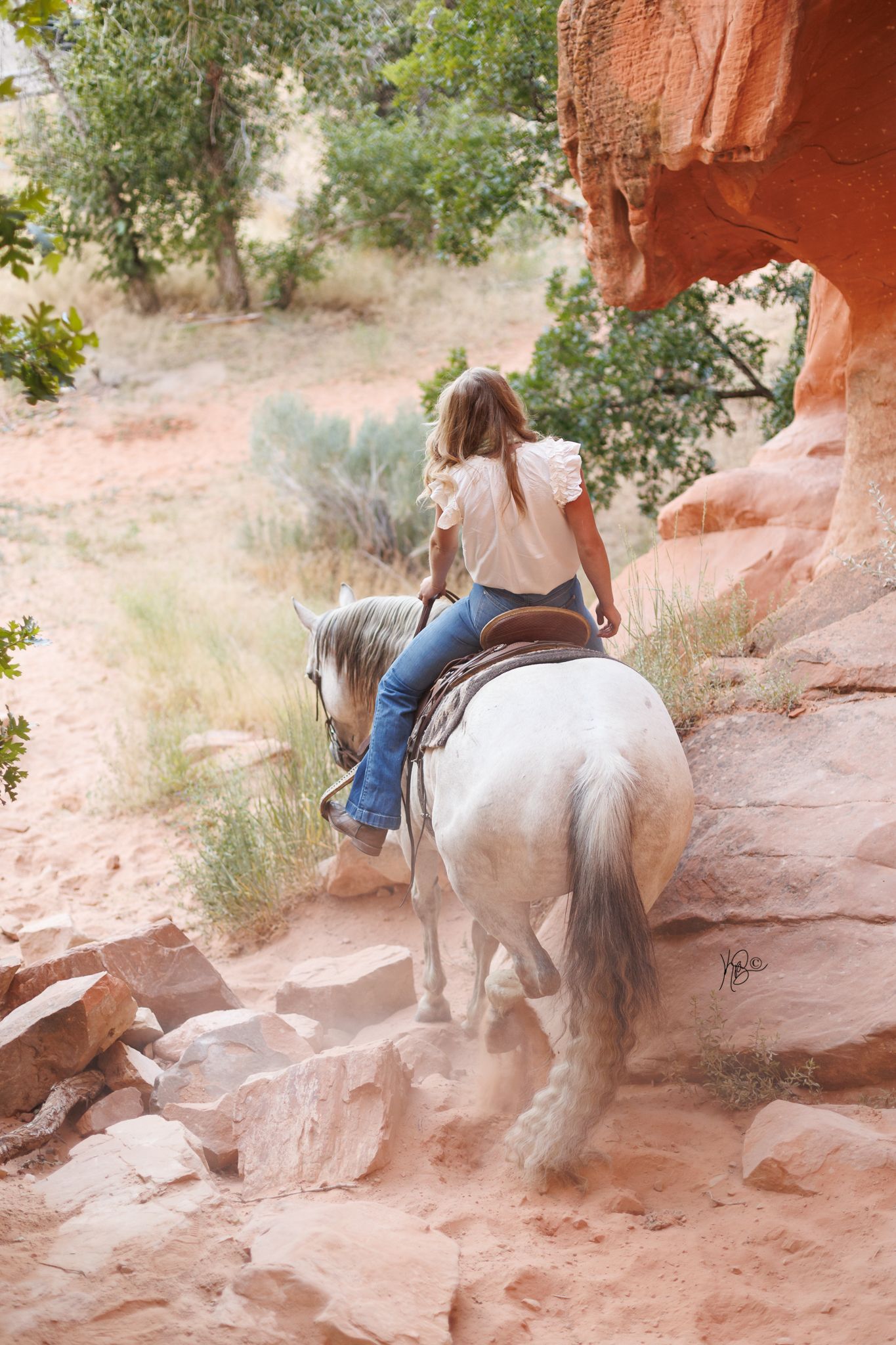 Horse and rider navigate rocky terrain on red sandstone cliffs.