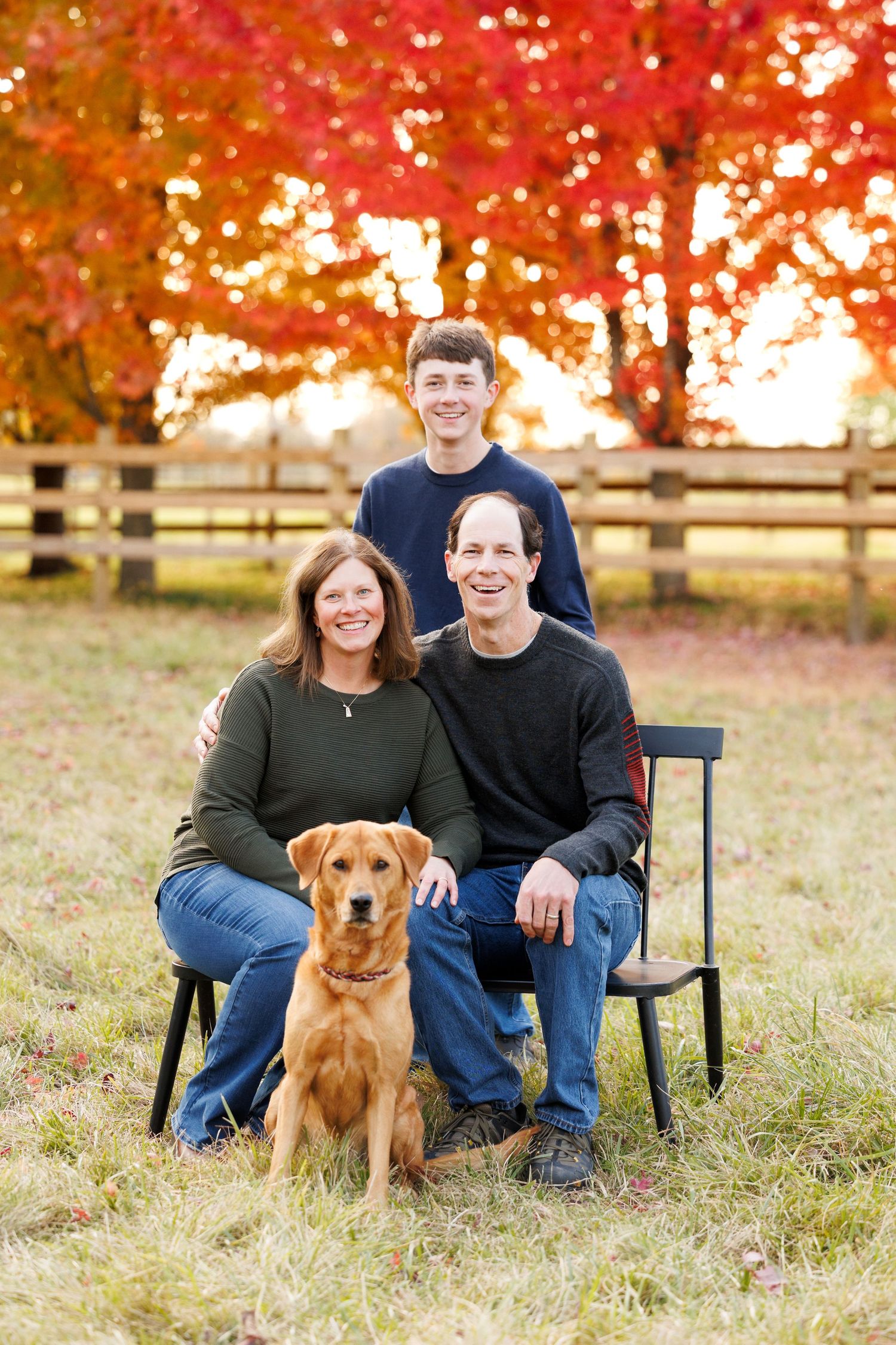 Family portrait with golden retriever during autumn with red maple trees in background.