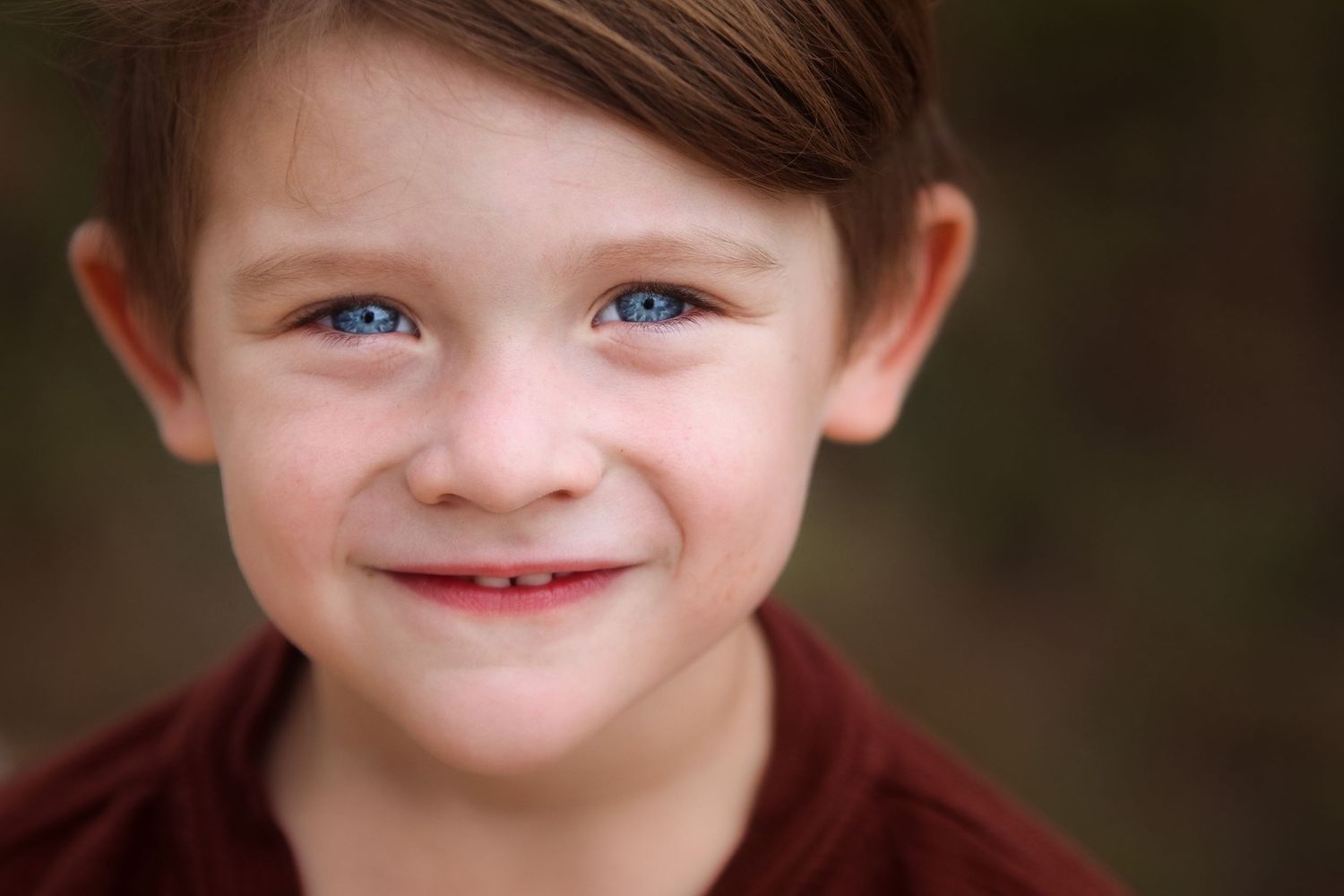 Close up portrait of a child with striking blue eyes wearing a burgundy sweater.