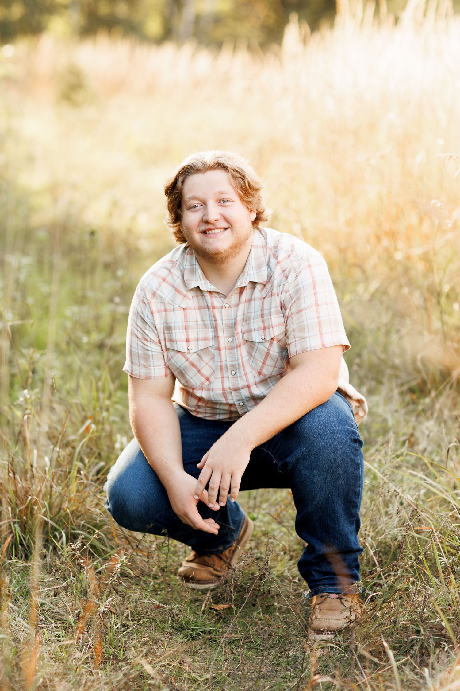 Outdoor senior session of a guy in tall grass during golden hour.