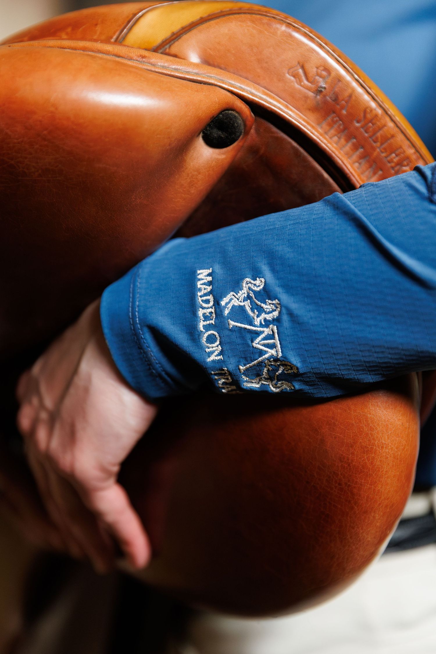 Close-up of a person in a blue Madelon equestrian shirt holding an english saddle.