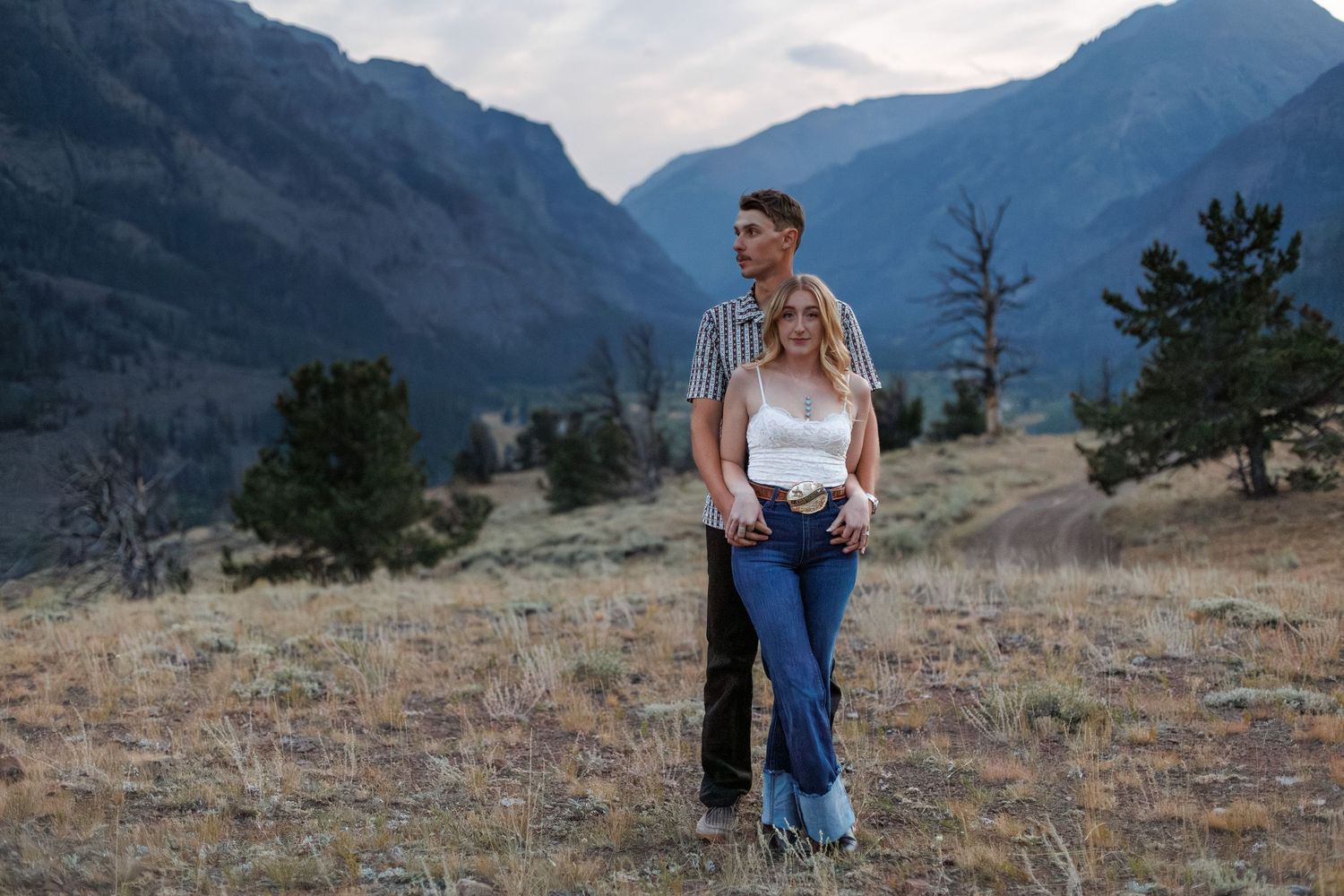A young couple embracing in rugged mountain landscape with dramatic peaks in background.