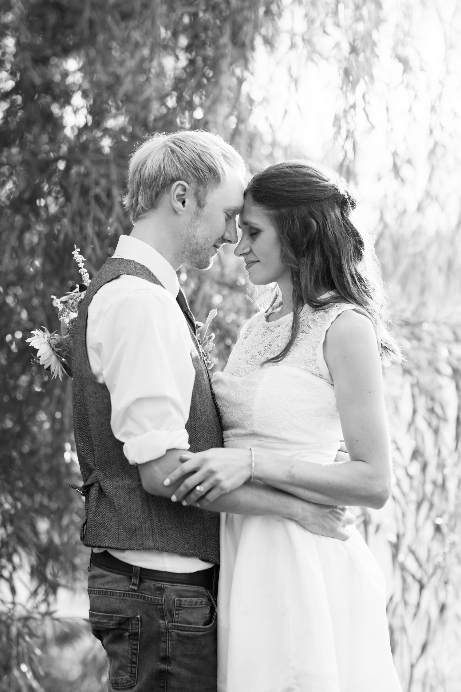 Black and white image of a newly married couple embracing in front of a willow tree