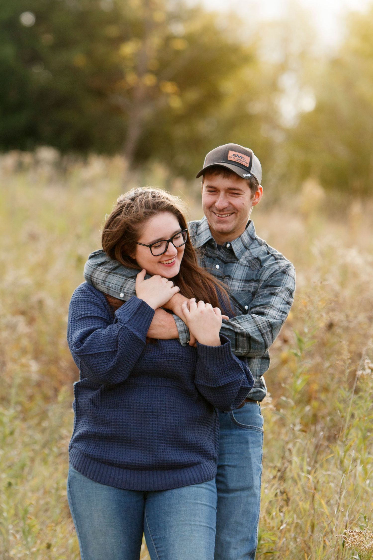Couple embracing and laughing in a sunlit field during golden hour.