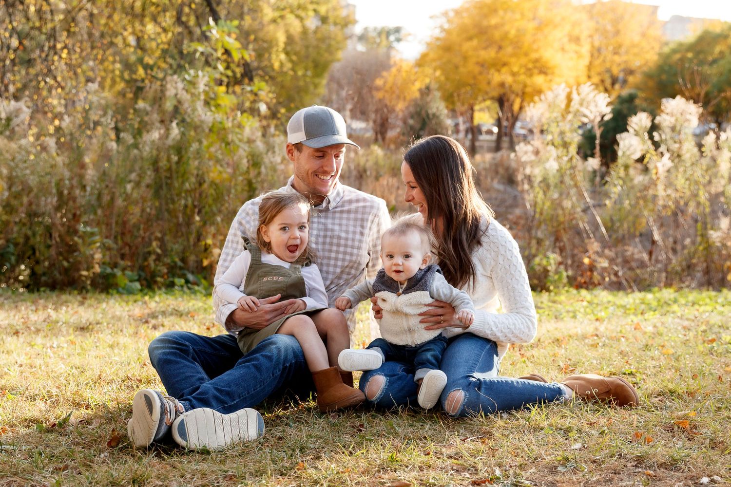 Family relaxing together on autumn grass during golden hour photo session.