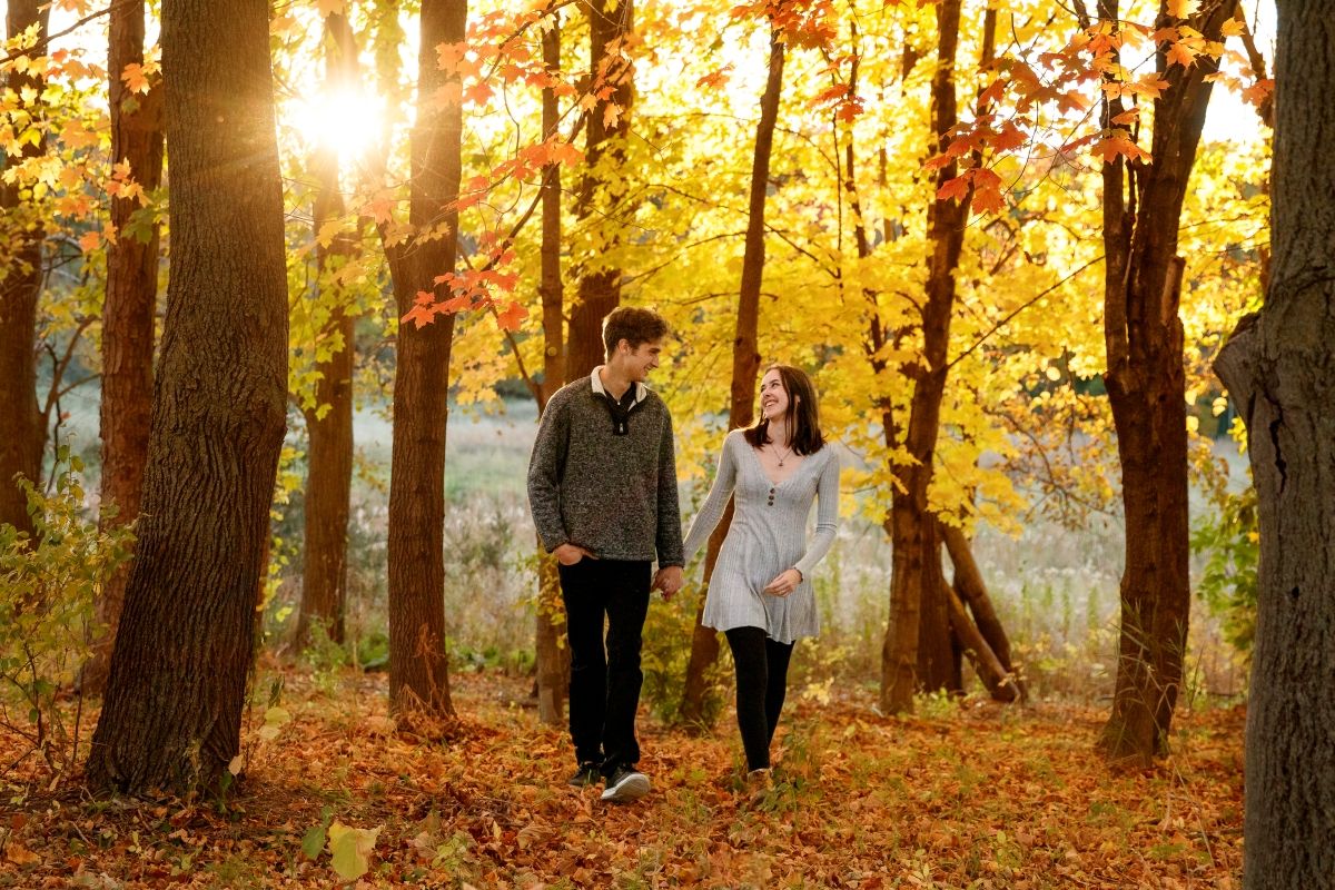 Couple walking together on a path through vibrant fall foliage with sunlight streaming through trees.
