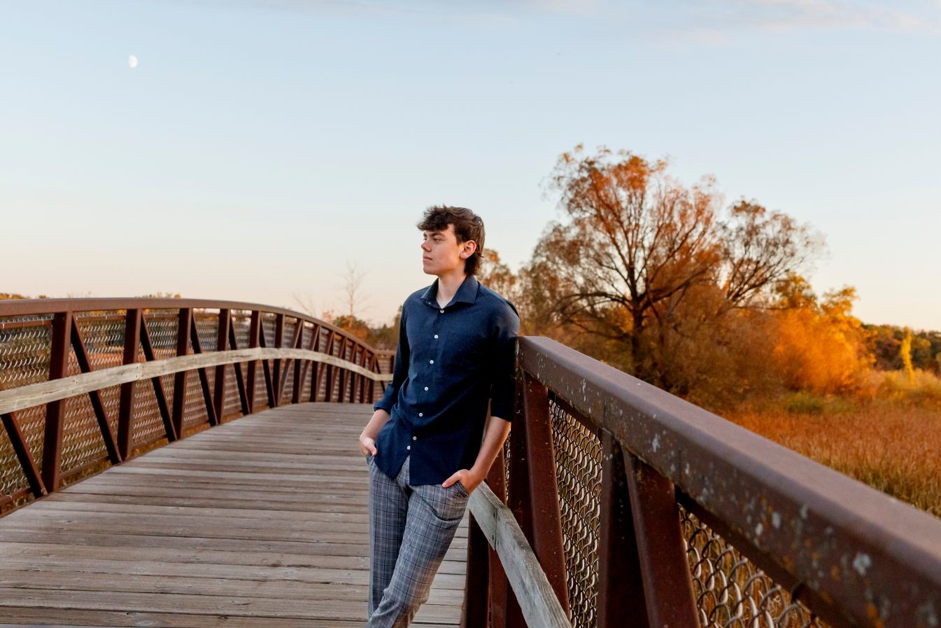Dramatic senior guy looking out into the distance on wooden bridge during golden hour.