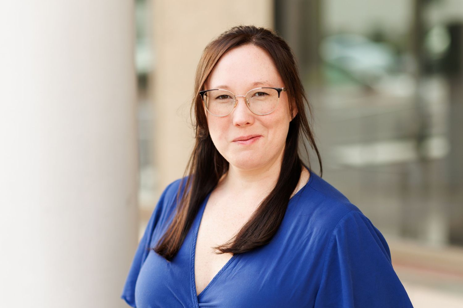 Professional headshot of woman in a bright blue top and glasses smiling warmly at the camera.