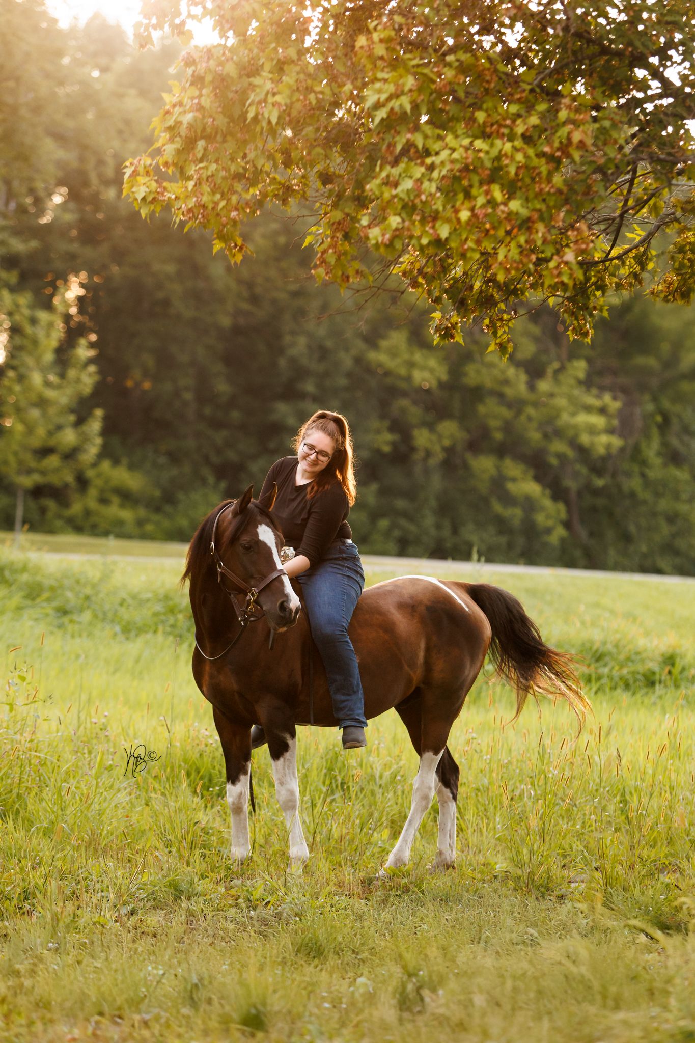 Woman riding her brown and white horse in a field at golden hour.