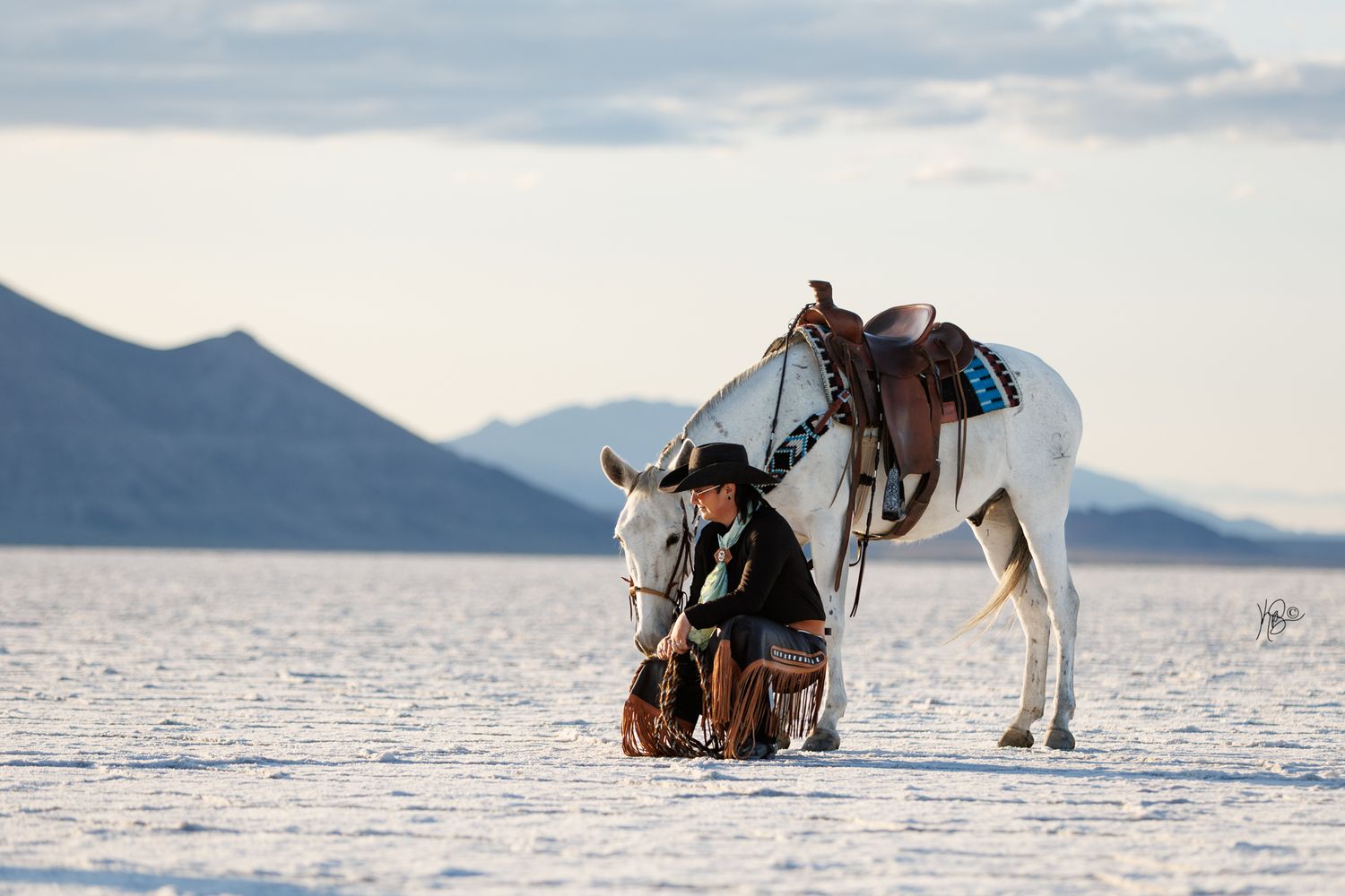 A woman kneeling down next to her grey mule in the salt flats.