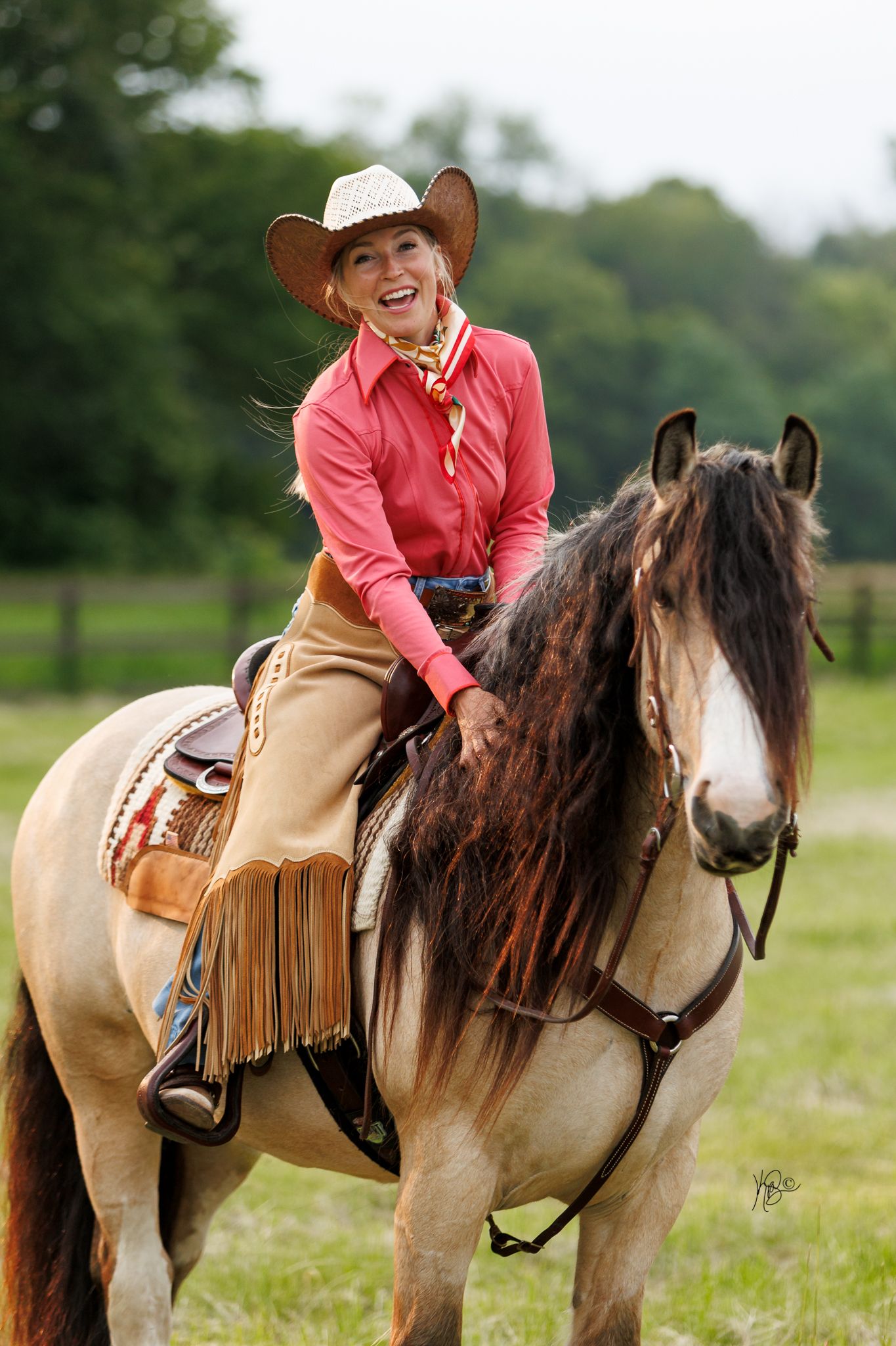 Equestrian woman laughing and petting her gypsy vanner's neck while riding.