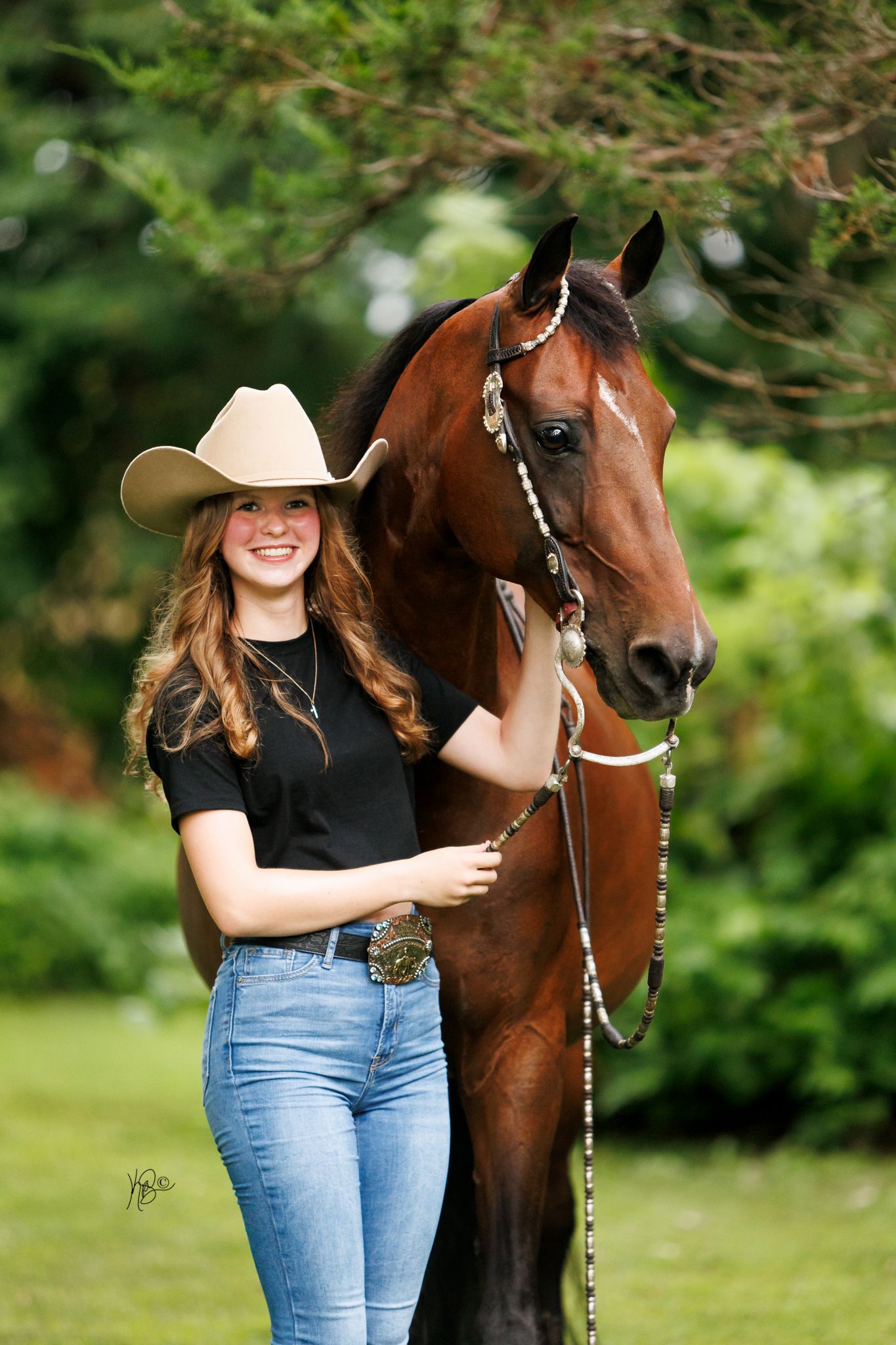 Western rider posing with her show horse for a portrait in a green setting.