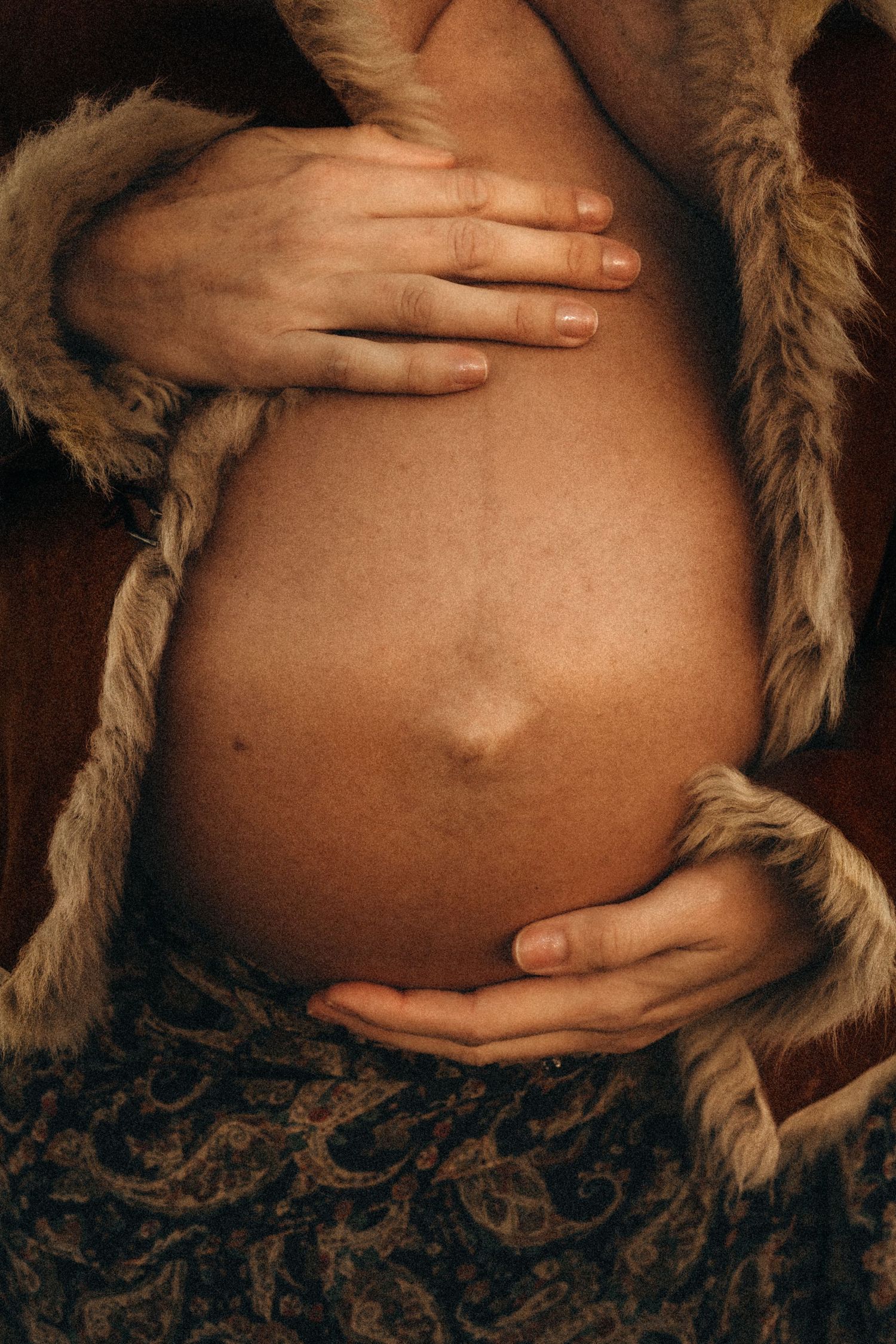 A series of maternity photos showing a pregnant belly with hands resting on it against a dark background with fur trim. Javea photographer