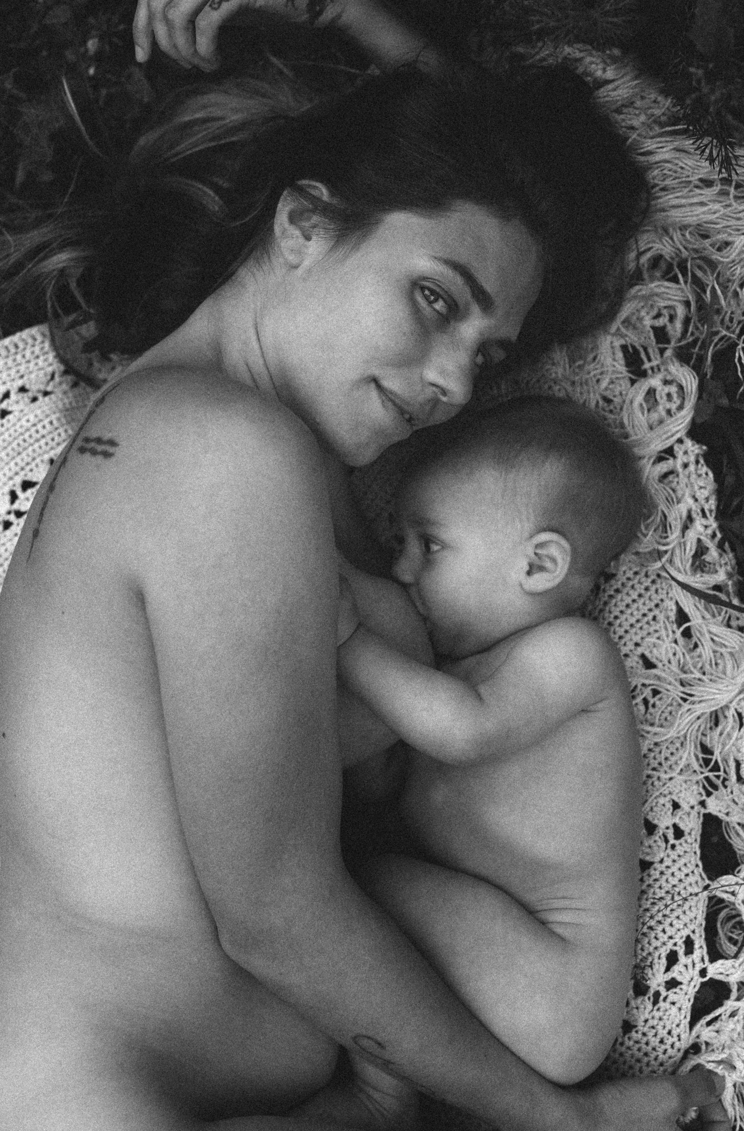 A tender black and white photograph of a parent and baby lying together on lace bedding. Javea photographer