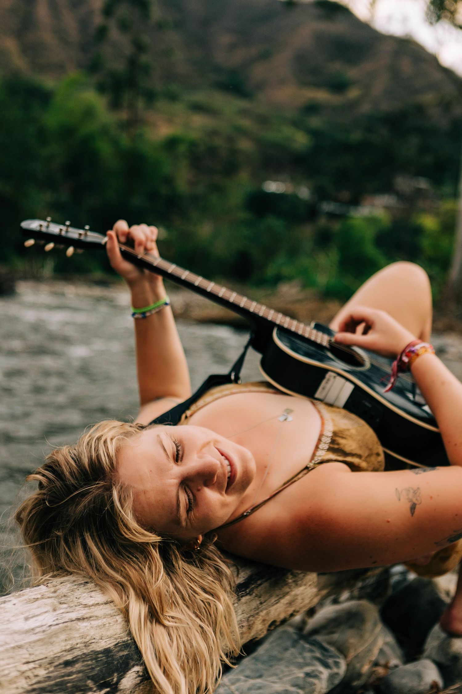 Solo photo session, girl laying on a log by a river on her back playing the guitar in Vilcabamba, Ecuador