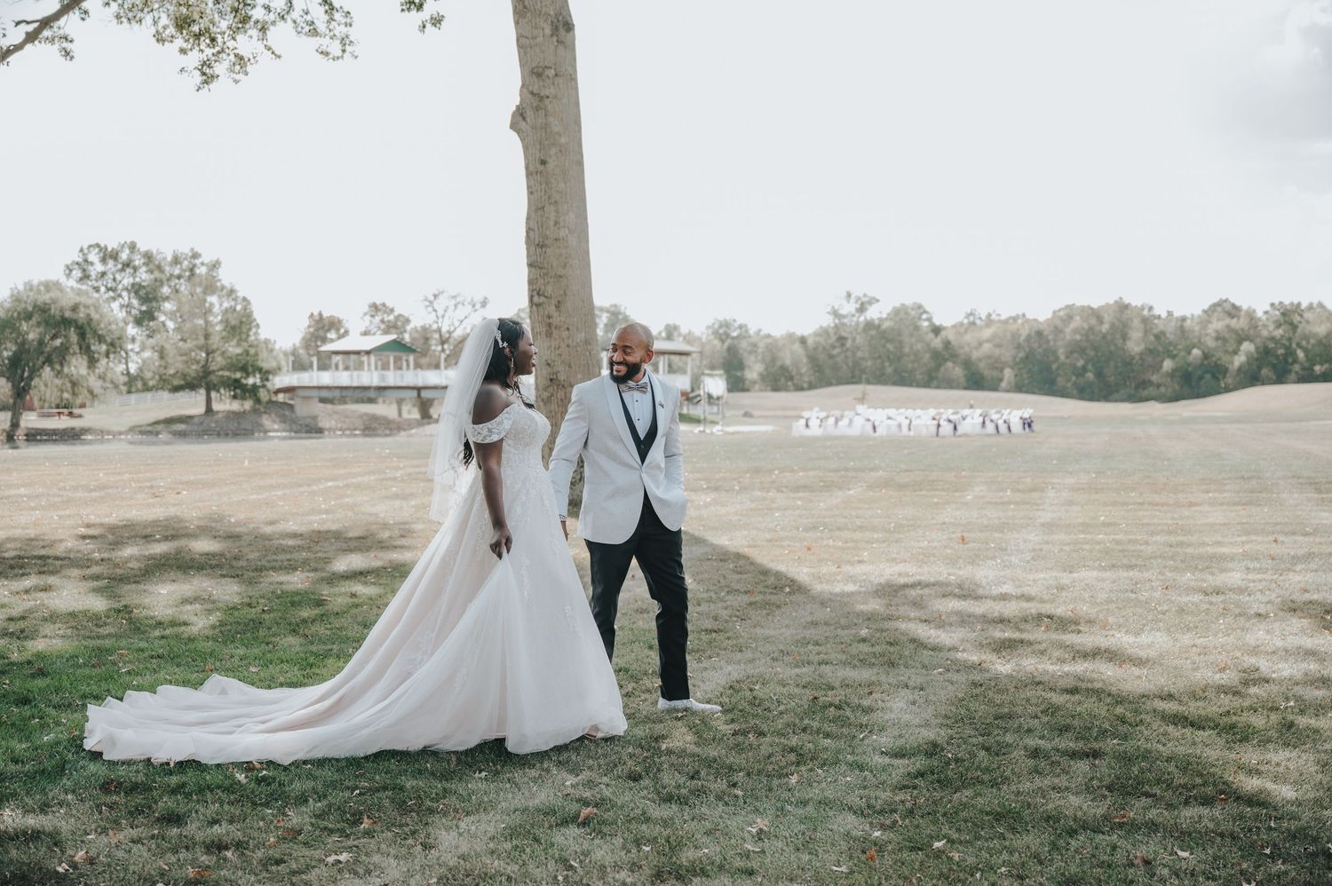 Wedding couple walking together through a scenic outdoor setting with trees and grass on a cloudy day.