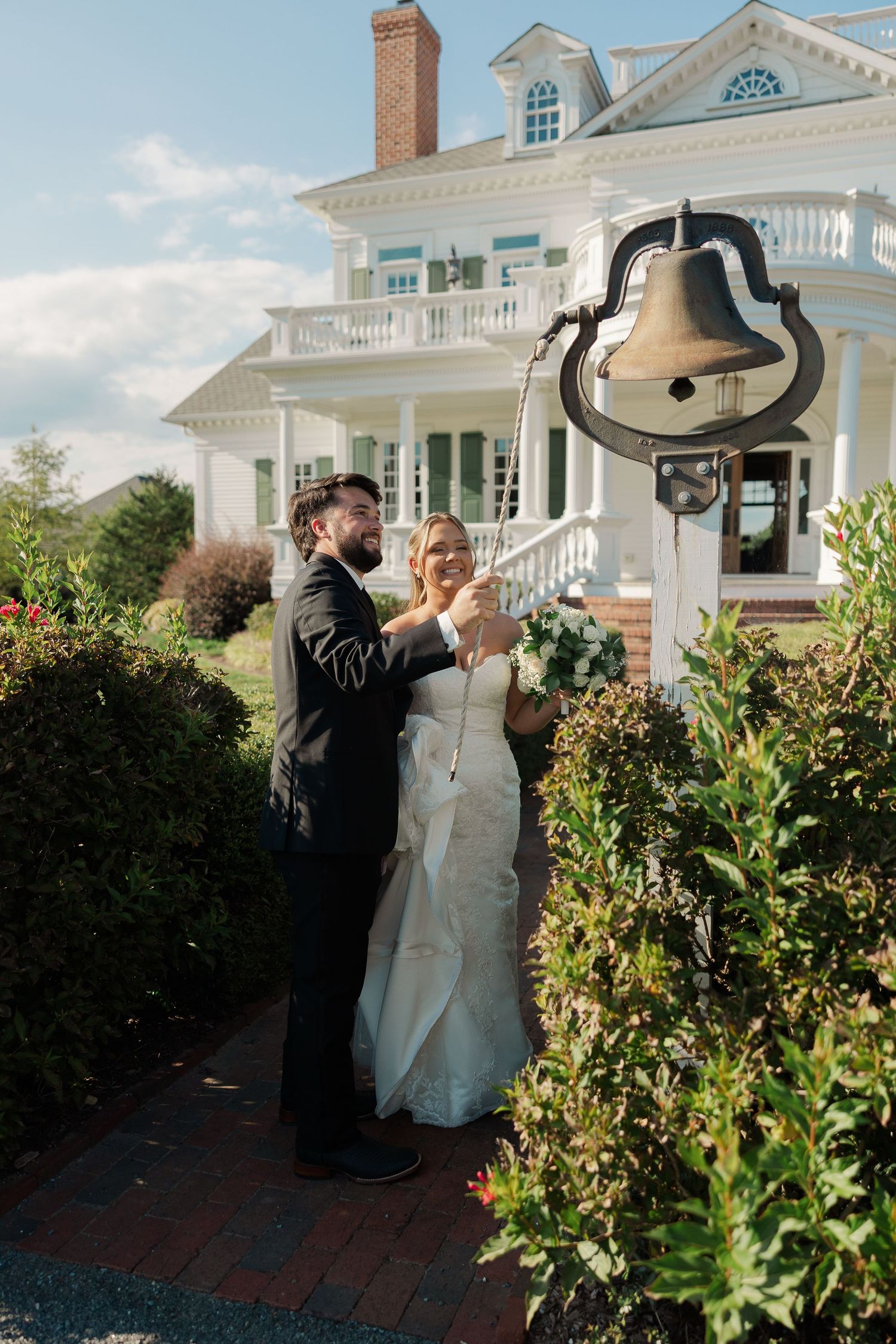 Bride and groom ringing a decorative bell outside a elegant white mansion on their wedding day.