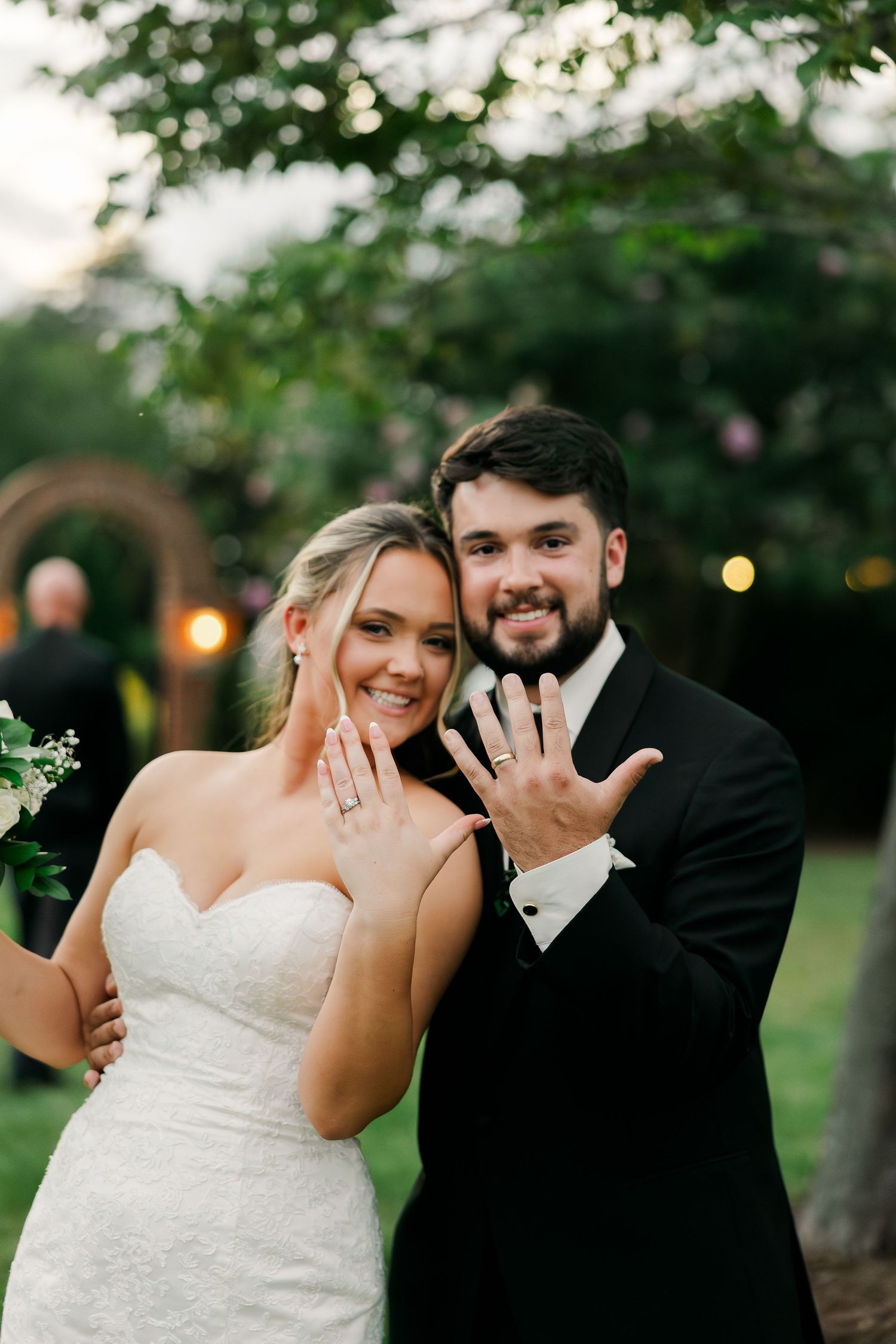 Bride and groom smiling and showing off wedding rings outdoors at garden wedding ceremony.