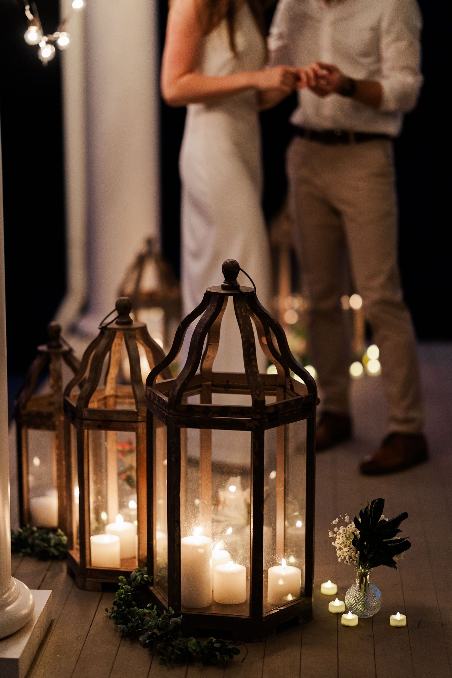 Rustic wooden lanterns with glowing candles illuminate an elegant outdoor wedding ceremony at night.
