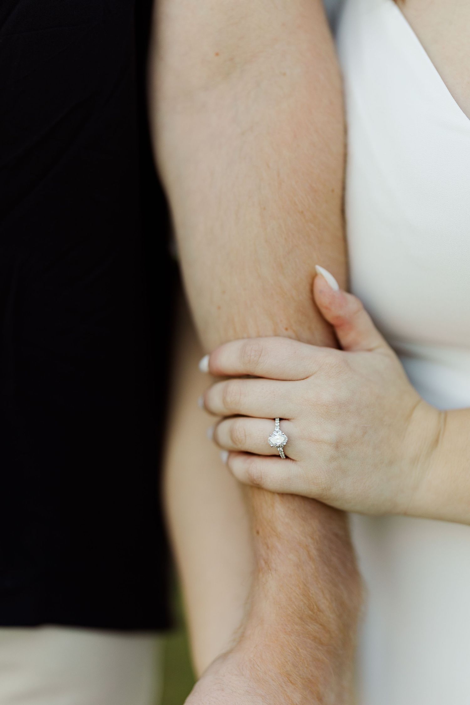 Close-up of a woman's hand with a diamond engagement ring resting on a man's arm, symbolizing love and commitment.