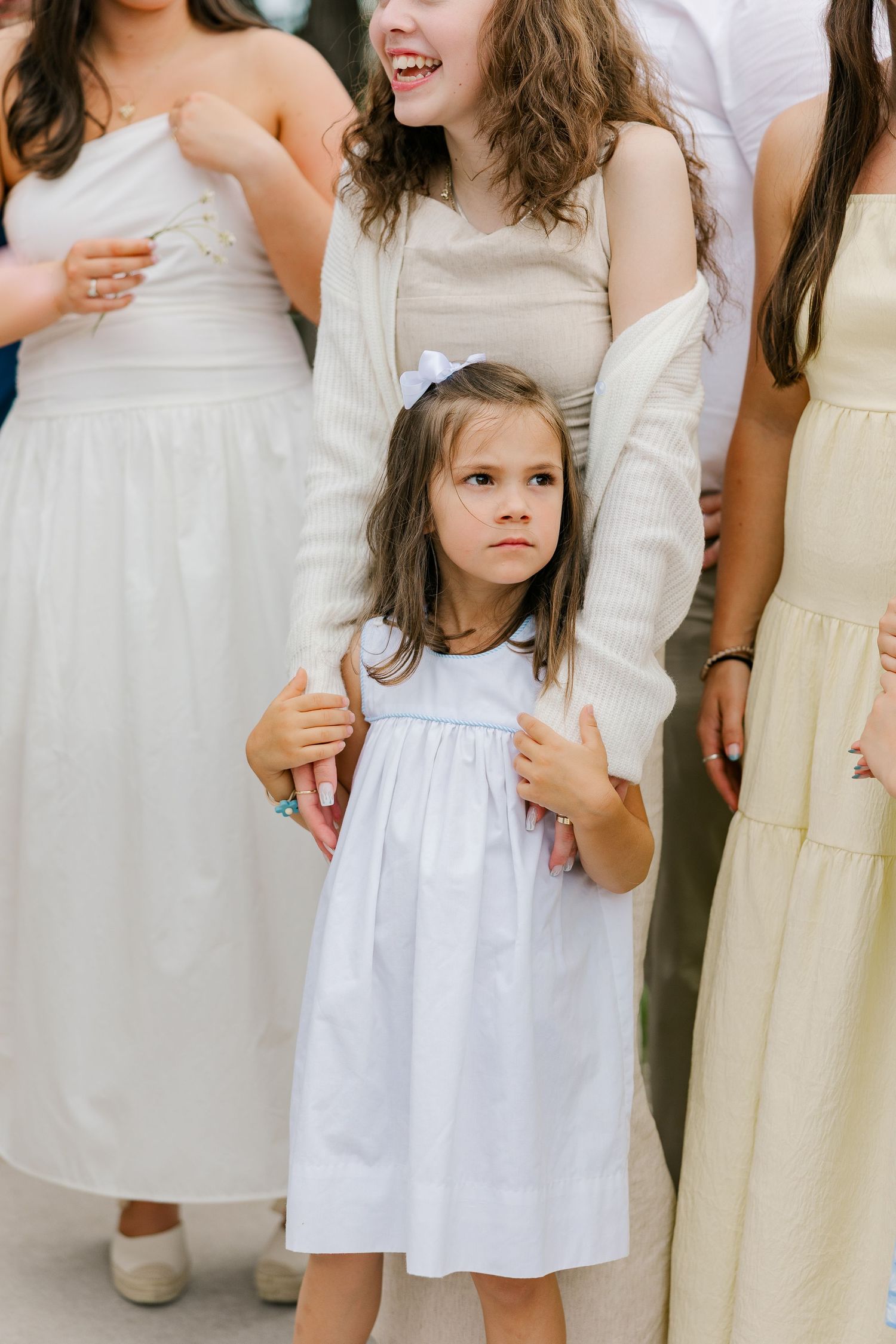 A group of young children in white and cream colored dresses stand together at a formal event.