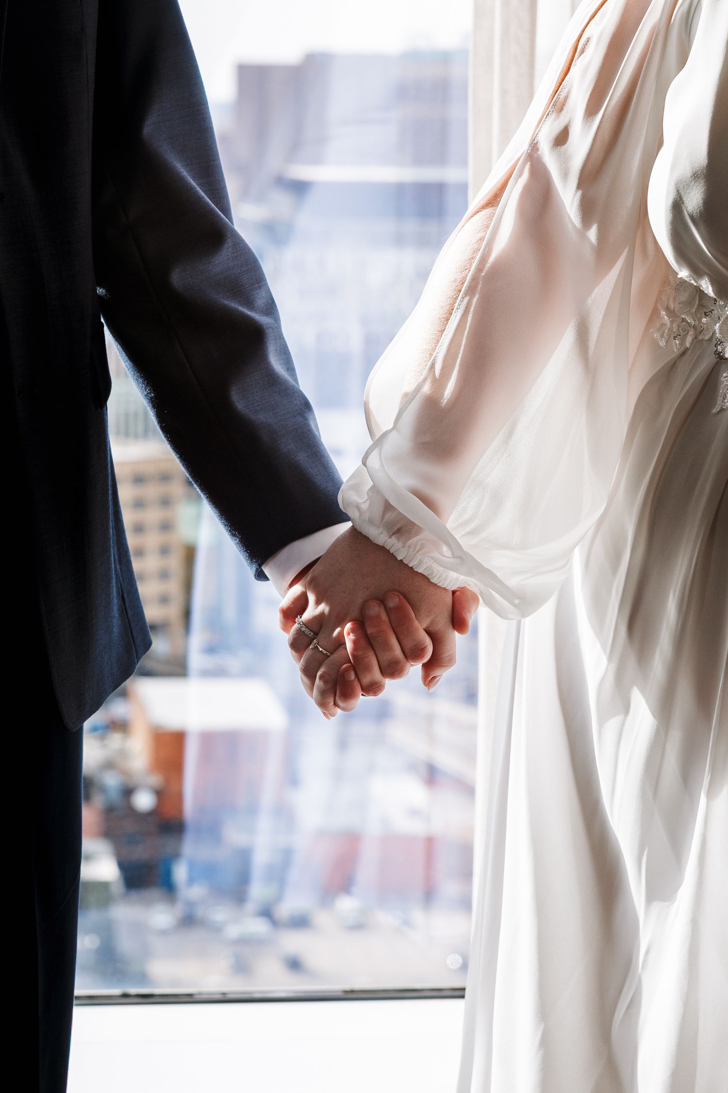 Couple holds hands overlooking a window of Downtown Detroit at the Greektown Hotel and Casino. Detroit Elopement Photographer