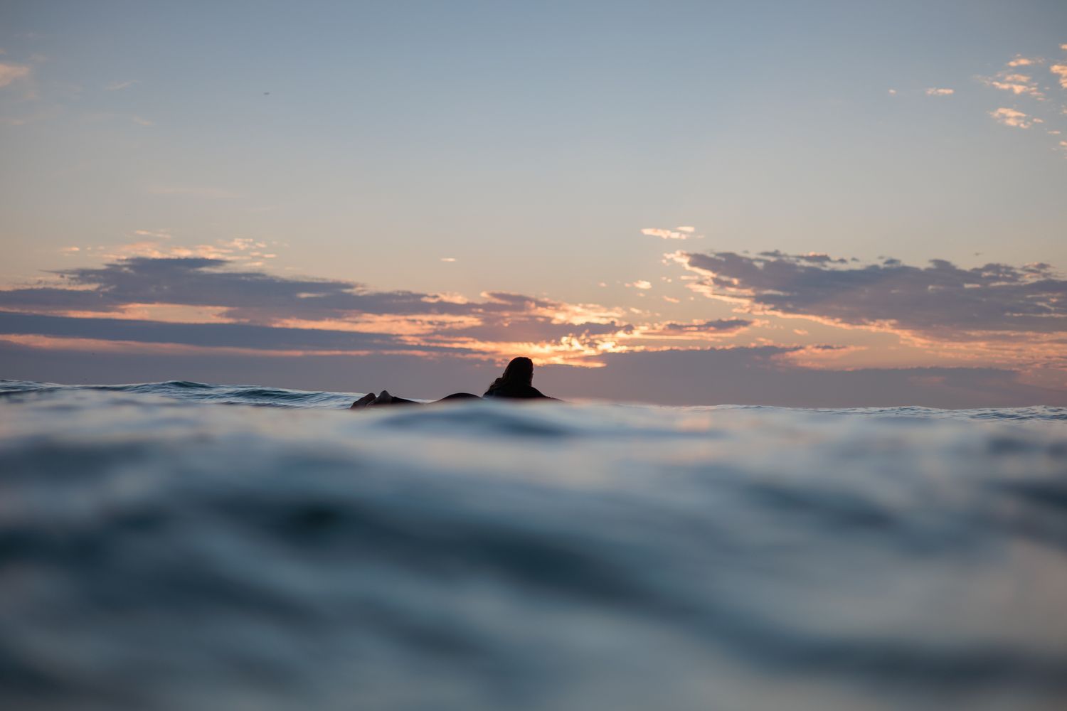 Surfer paddling out a sunrise