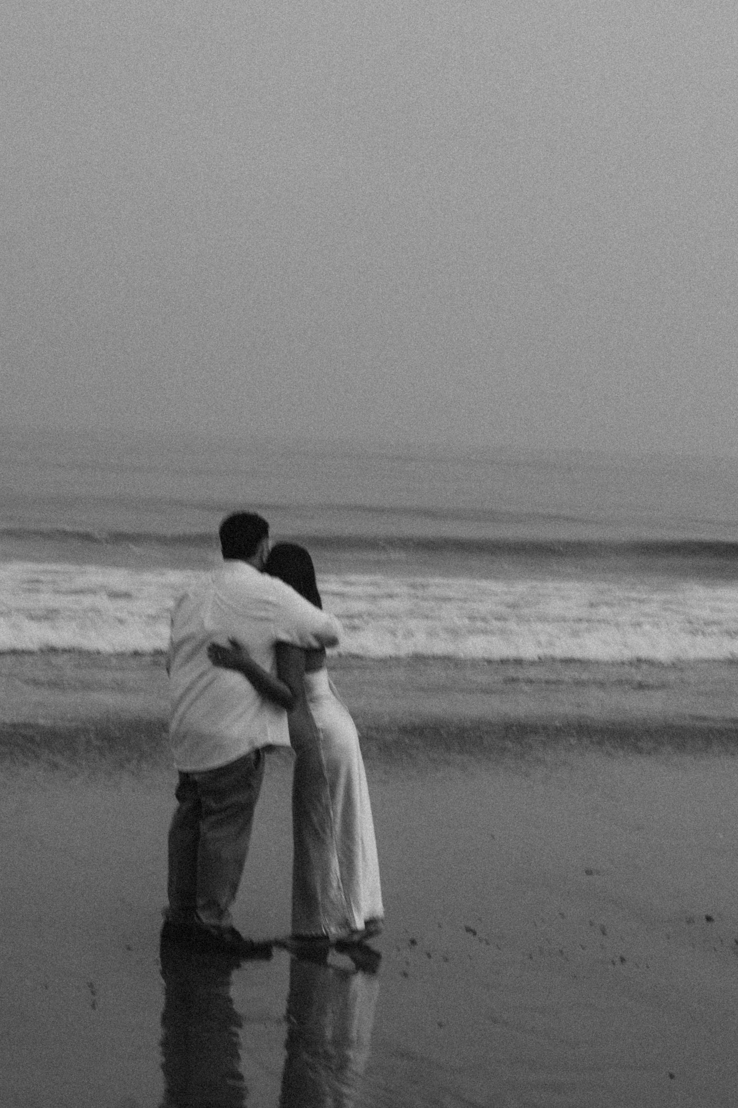 Grainy black and white photo of a couple embracing, unposed and honest, with soft light.