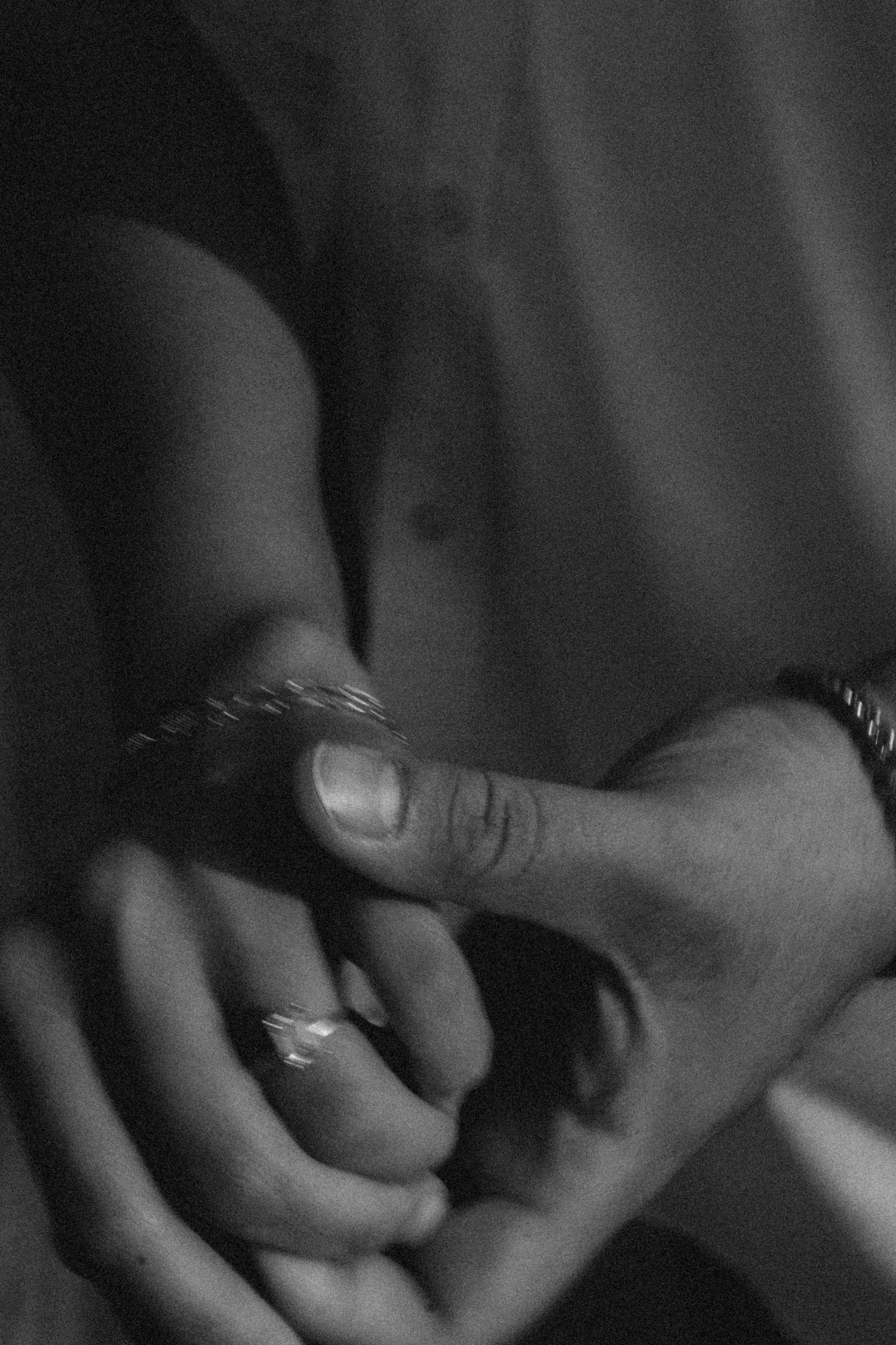 Black and white detail photo of intertwined hands, soft grain and blur reflecting quiet love.