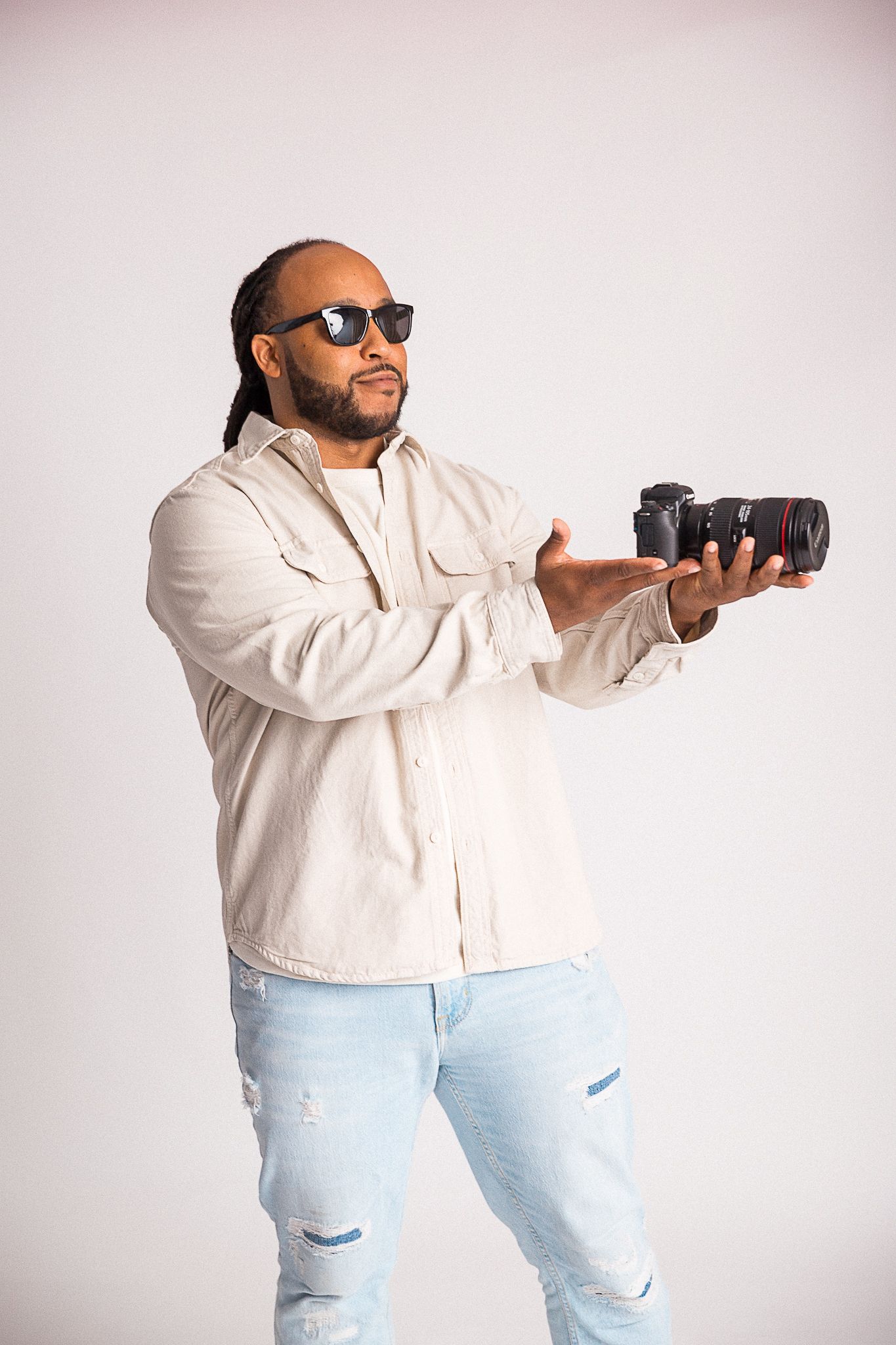 Photographer in casual wear demonstrating camera handling technique against white background.