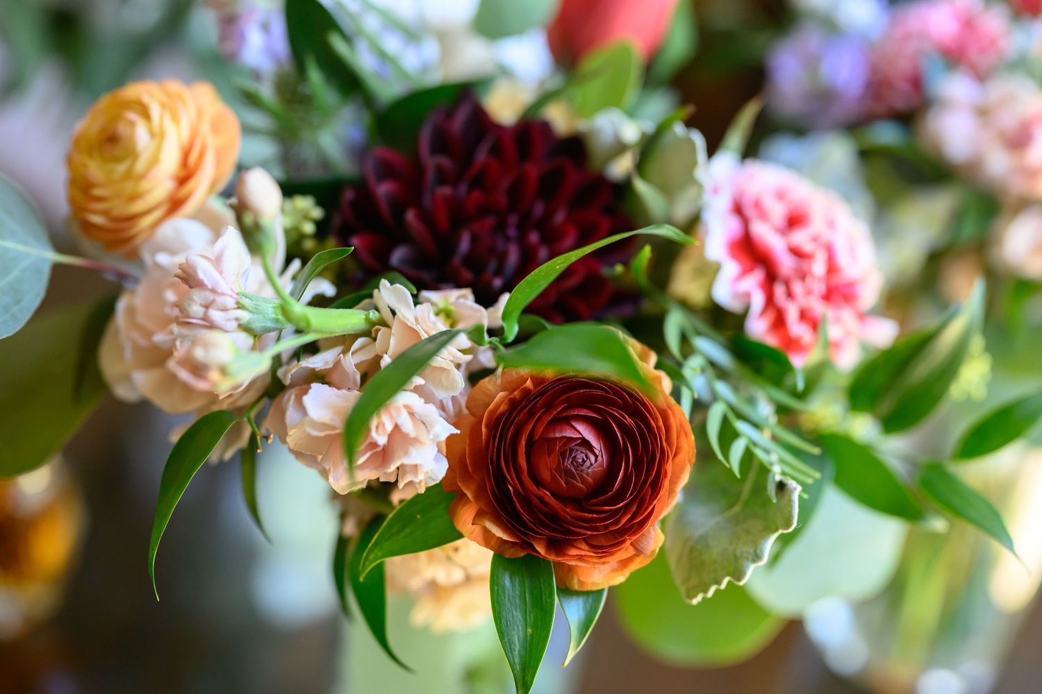 Vibrant mixed floral arrangement featuring ranunculus, dahlias, and greenery in warm autumn tones.