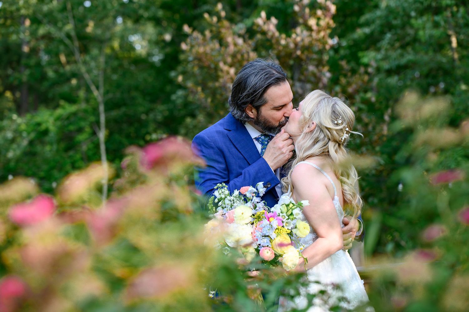 Bride and groom sharing a romantic kiss in a lush garden, surrounded by colorful blooms during their wedding day.