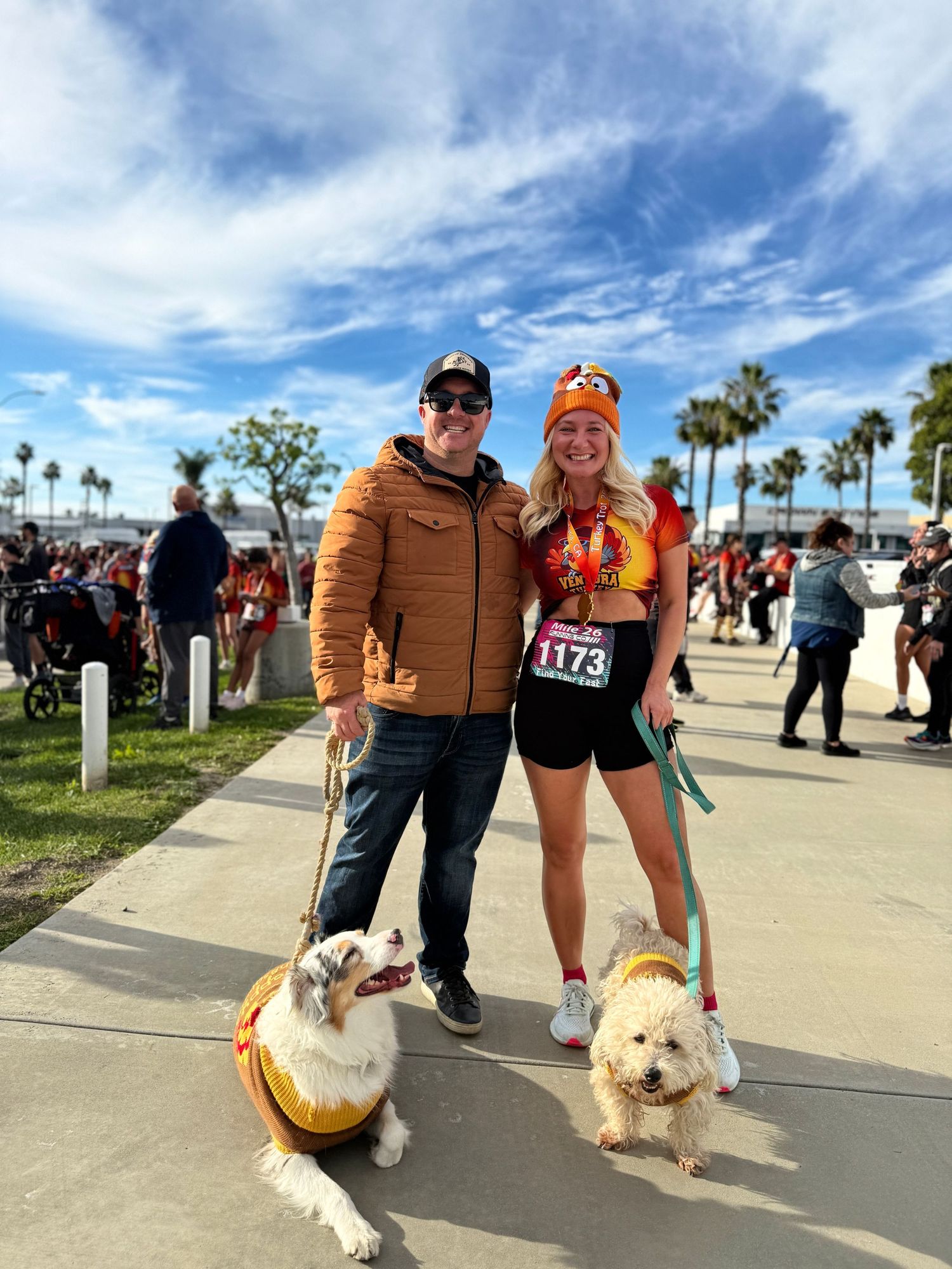People walking dogs along a sunny beachfront promenade with palm trees in the background.