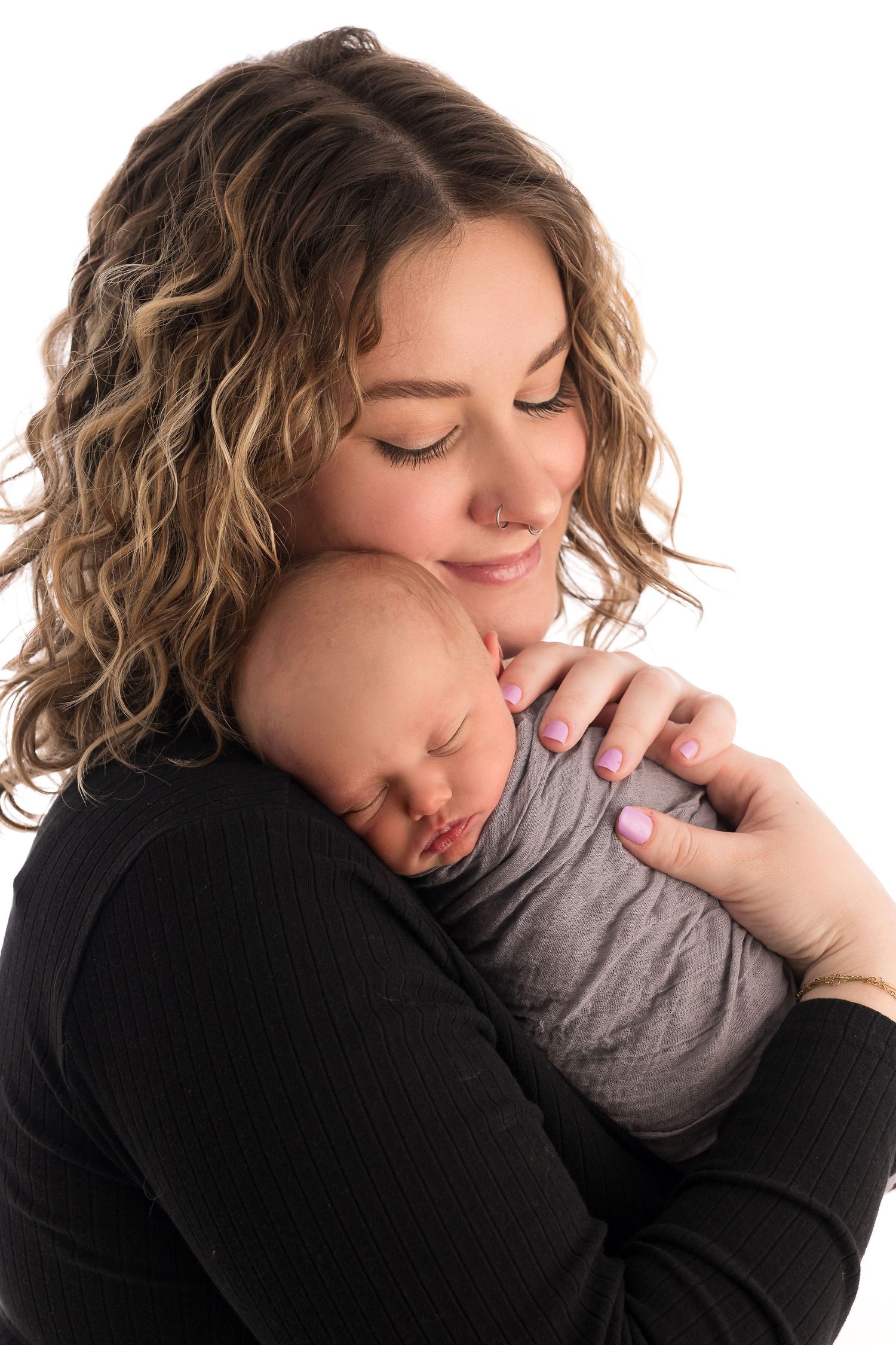 A tender moment captured as mother in black sweater holds sleeping baby in gray outfit.