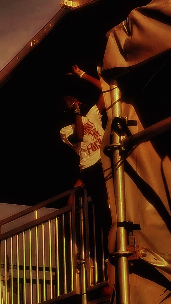 Performer on stage stairs pointing upward wearing a white graphic tee under dramatic lighting.