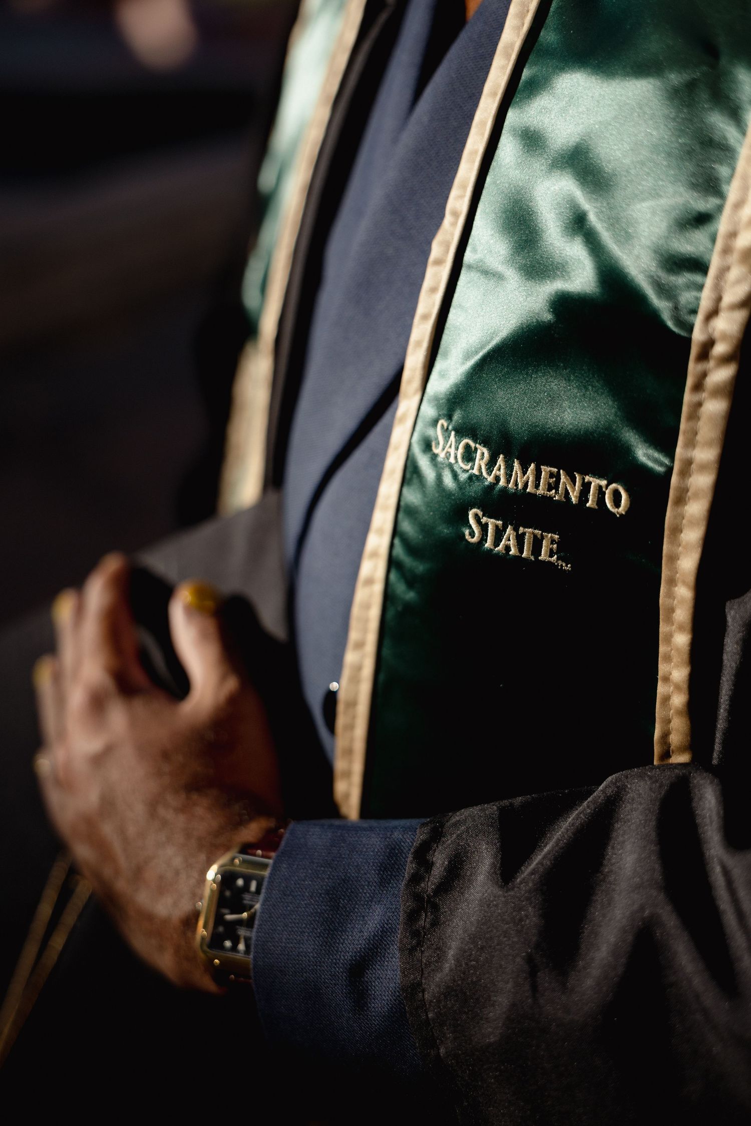 Close-up of Sacramento State graduation regalia with green and gold satin hood worn during commencement ceremony.