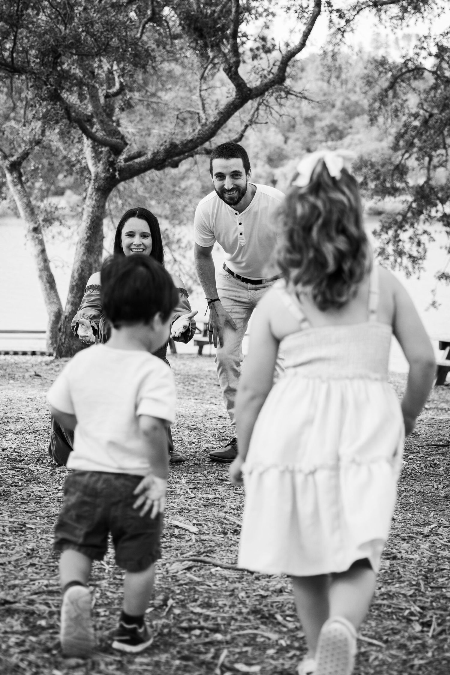 Black and white photo of a happy family playing together in a park, with two children running toward their smiling parents.